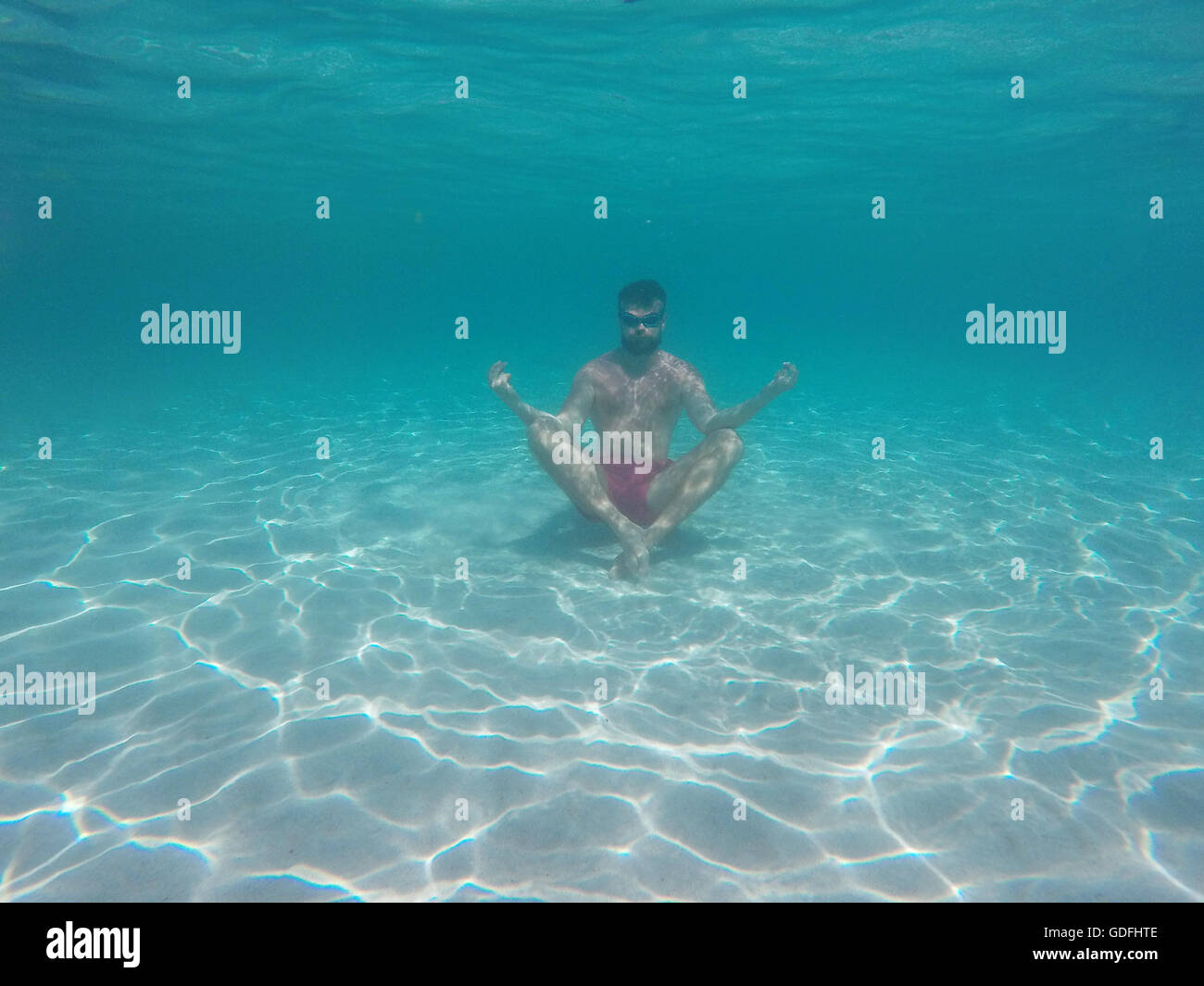 Junger Bart Mann mit Brille im Lotussitz meditieren unter Wasser Stockfoto