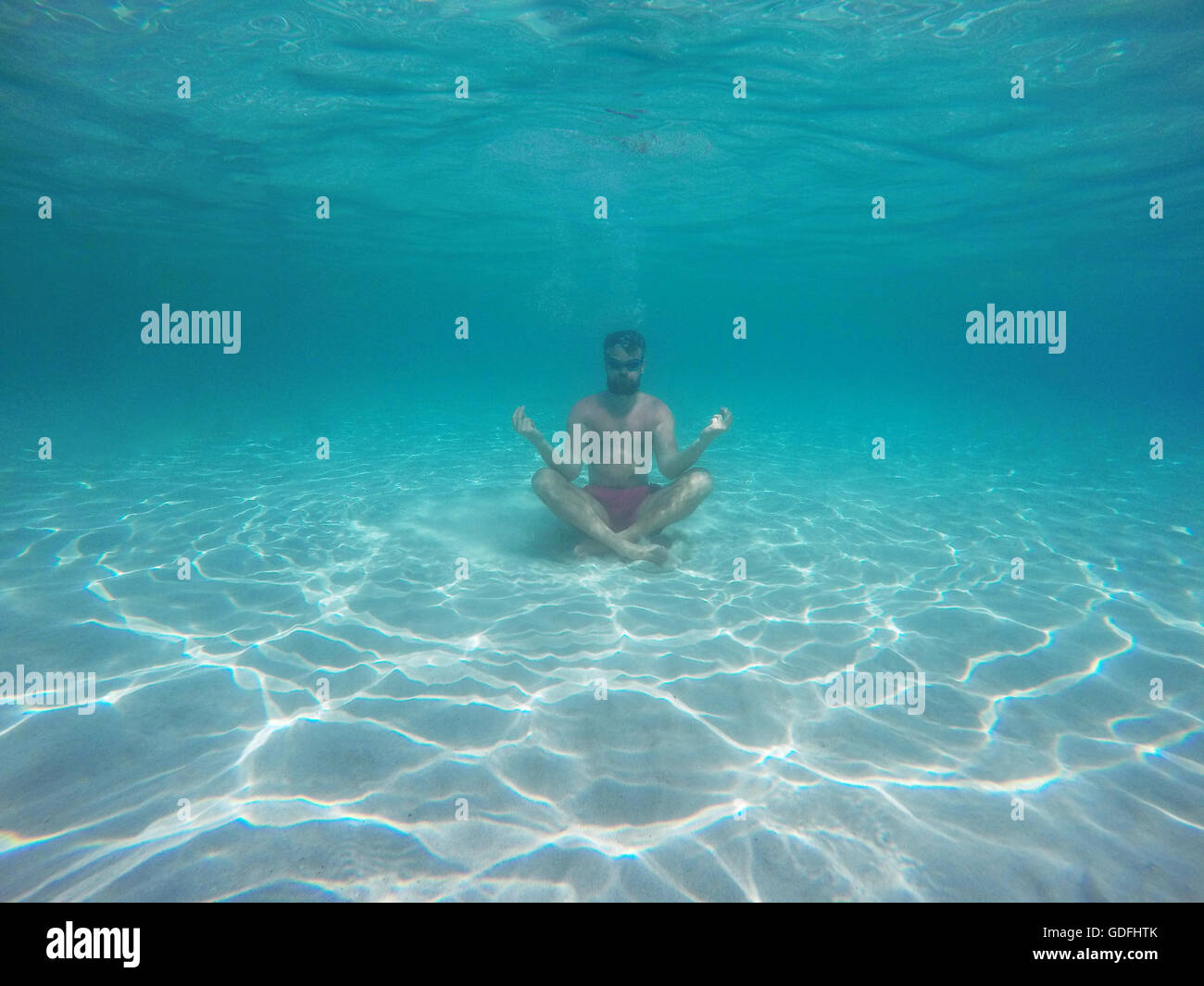 Junger Bart Mann mit Brille im Lotussitz meditieren unter Wasser Stockfoto