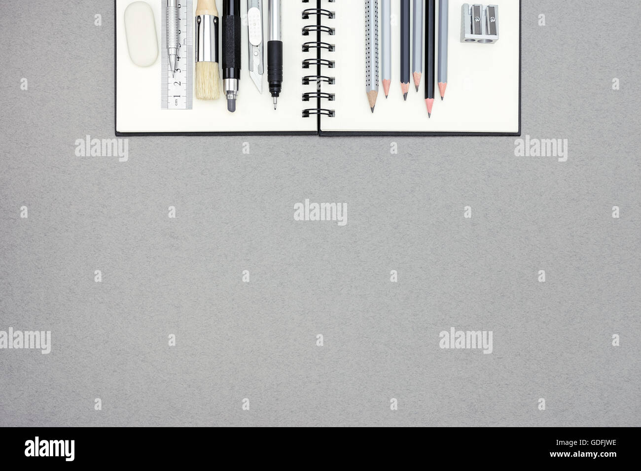 Spiral-Notizbuch und verschiedene Zeichenwerkzeuge auf grau Recycling-Papierhintergrund, Ansicht von oben Stockfoto