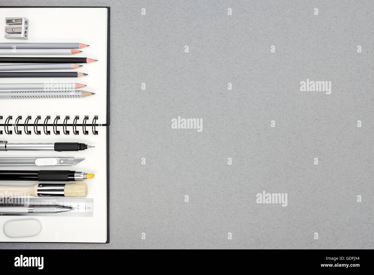 Spiral-Notizbuch und verschiedene Zeichenwerkzeuge auf grauen Recyclingpapier Hintergrund, Ansicht von oben Stockfoto