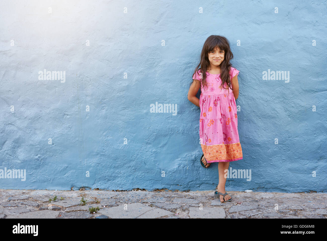 In voller Länge Portrait von hübsches kleines Mädchen Blick in die Kamera und lächelnd stehend gegen blaue Wand mit Textfreiraum Stockfoto