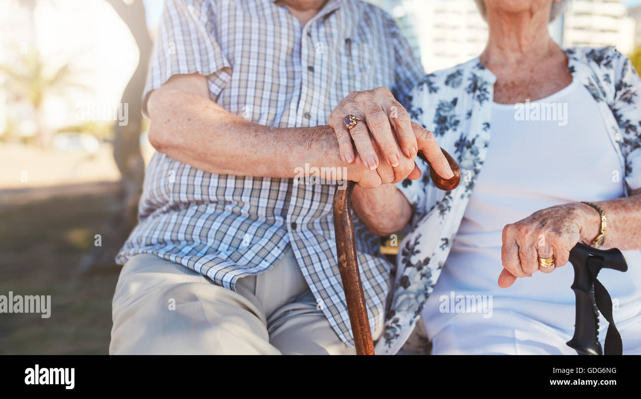 Nahaufnahme von älteres paar Hand in Hand beim Sitzen auf der Parkbank zusammen. Pensionierter Mann und Frau mit dem Rohrstock zu gehen. Fokus Stockfoto