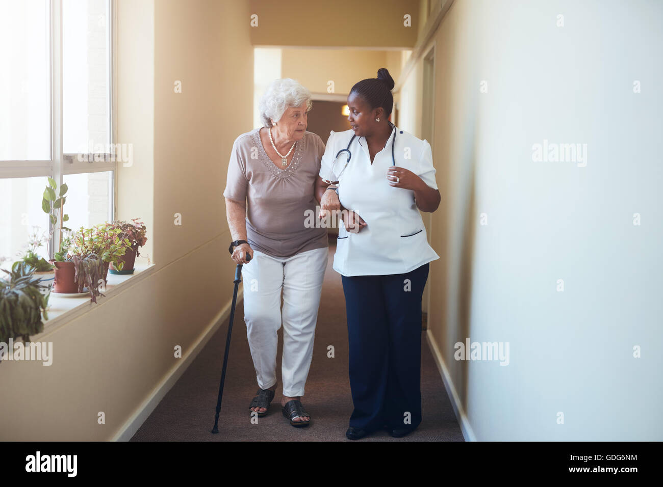 Ältere Frau mit Gehstock von einer Krankenschwester zu Hause geholfen. Volle Länge-Schuss der Ärztin mit älteren Patienten ein Stockfoto