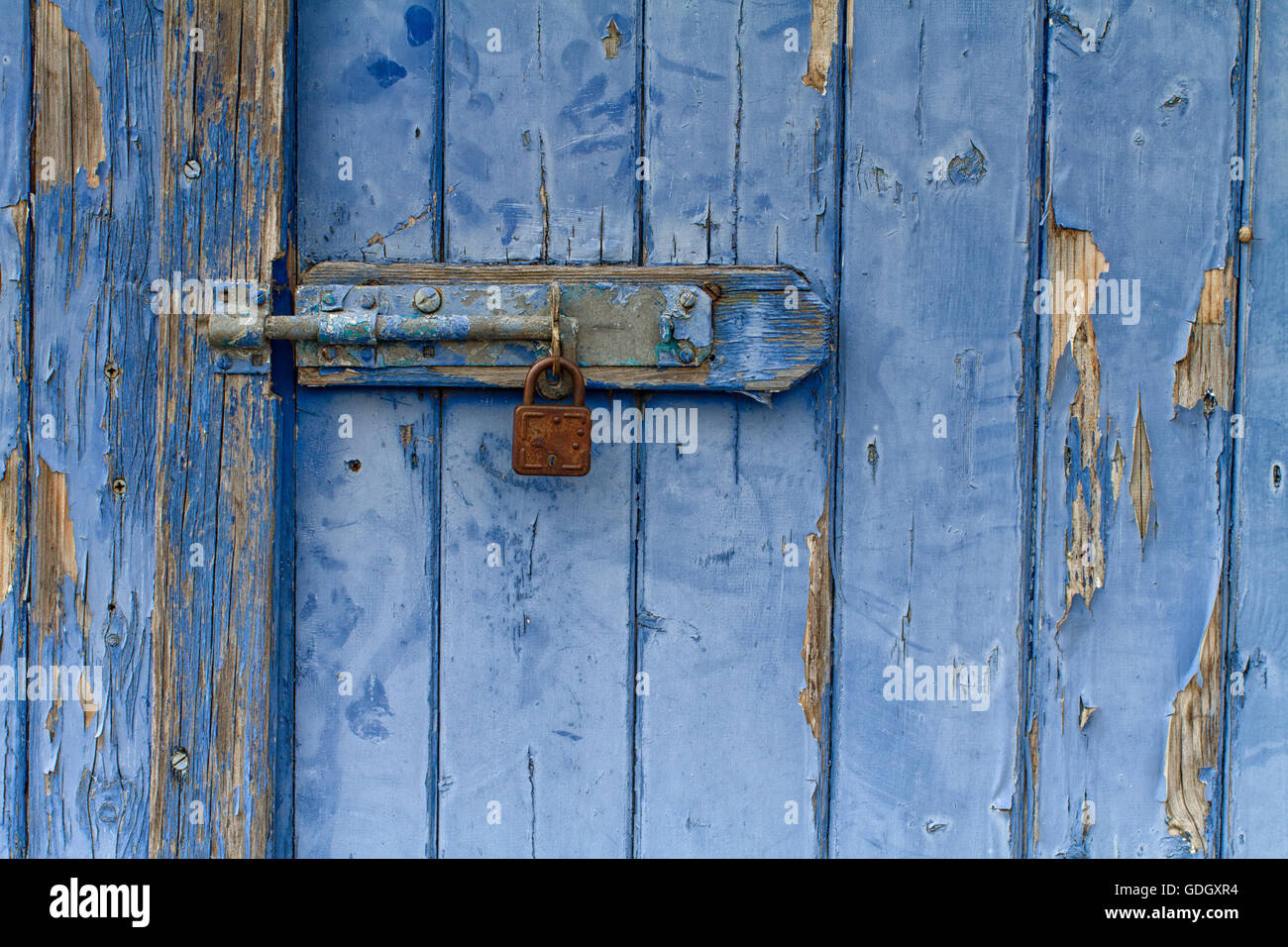Abblätternde blau bemalte Holztür mit rostigen Vorhängeschloss Stockfoto