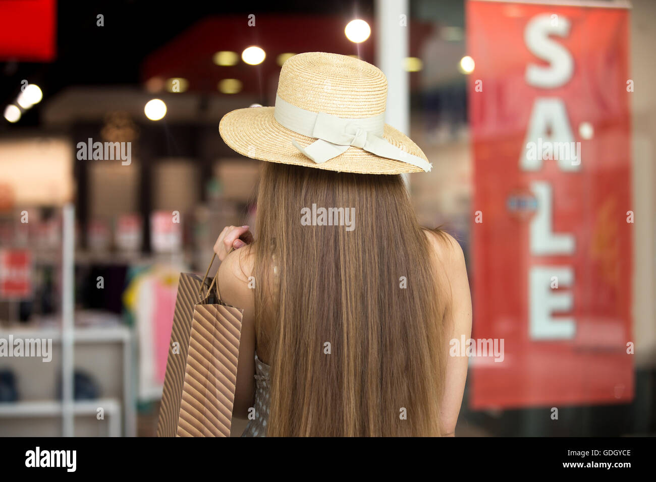 Junge hübsche stilvolle langhaarige Frau Hut im Einkaufszentrum, Wandern im Bekleidungsgeschäft, braune Shopping Tasche halten Stockfoto