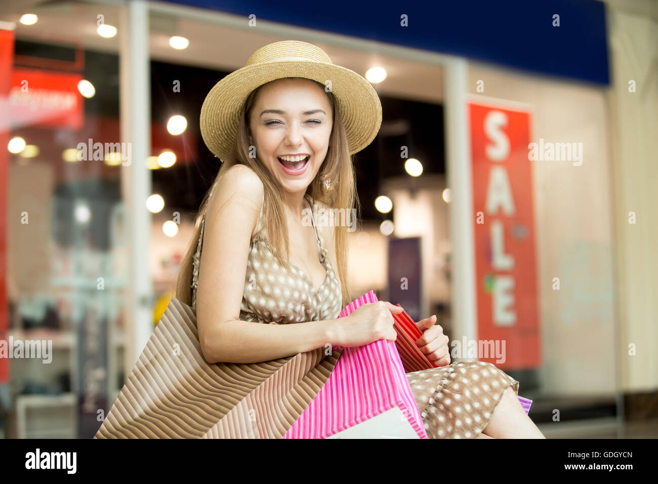 Porträt der fröhliche junge hübsche Frau mit Hut im Einkaufszentrum, umarmt fest Taschen mit Einkäufen, fröhlich lachend Stockfoto