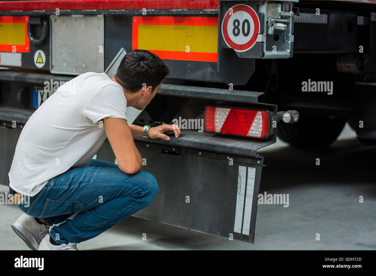 Junge Mechaniker Inspektion LKW auf der Rückseite, Blick auf Räder und Getriebe Stockfoto