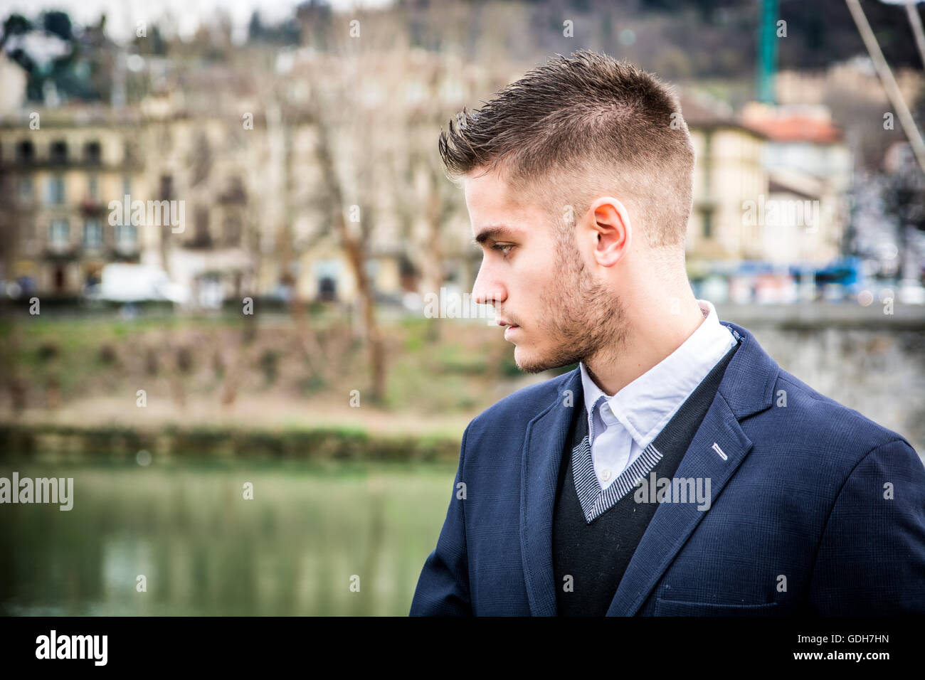 3/4 Länge des kontemplativen leichte Braunhaarige junge Mann trägt graue Jacke und Denim Jeans stehend neben umge Stockfoto