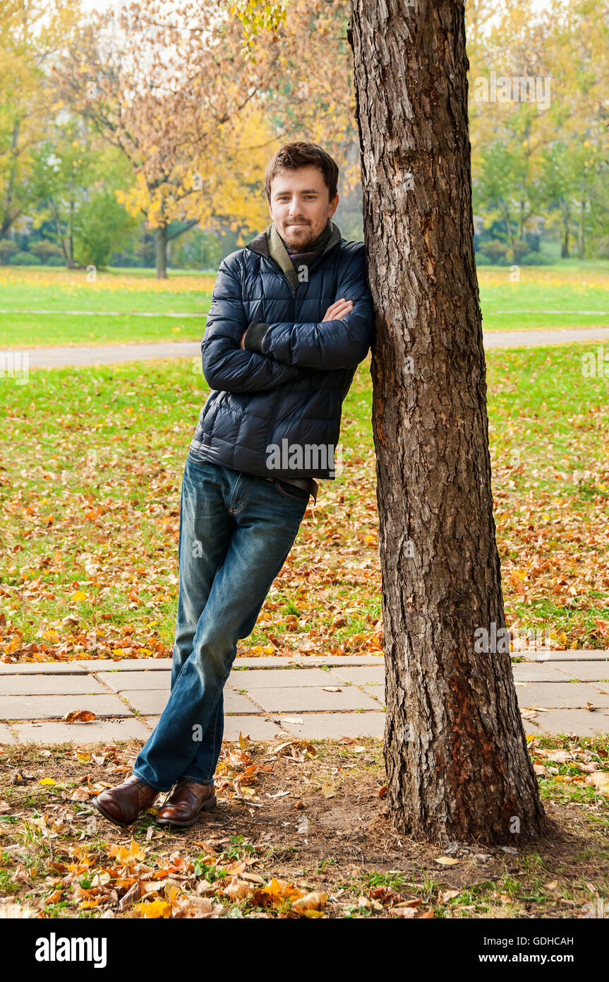 Hübscher Kerl lehnte sich gegen einen Baum im Herbst park Stockfoto