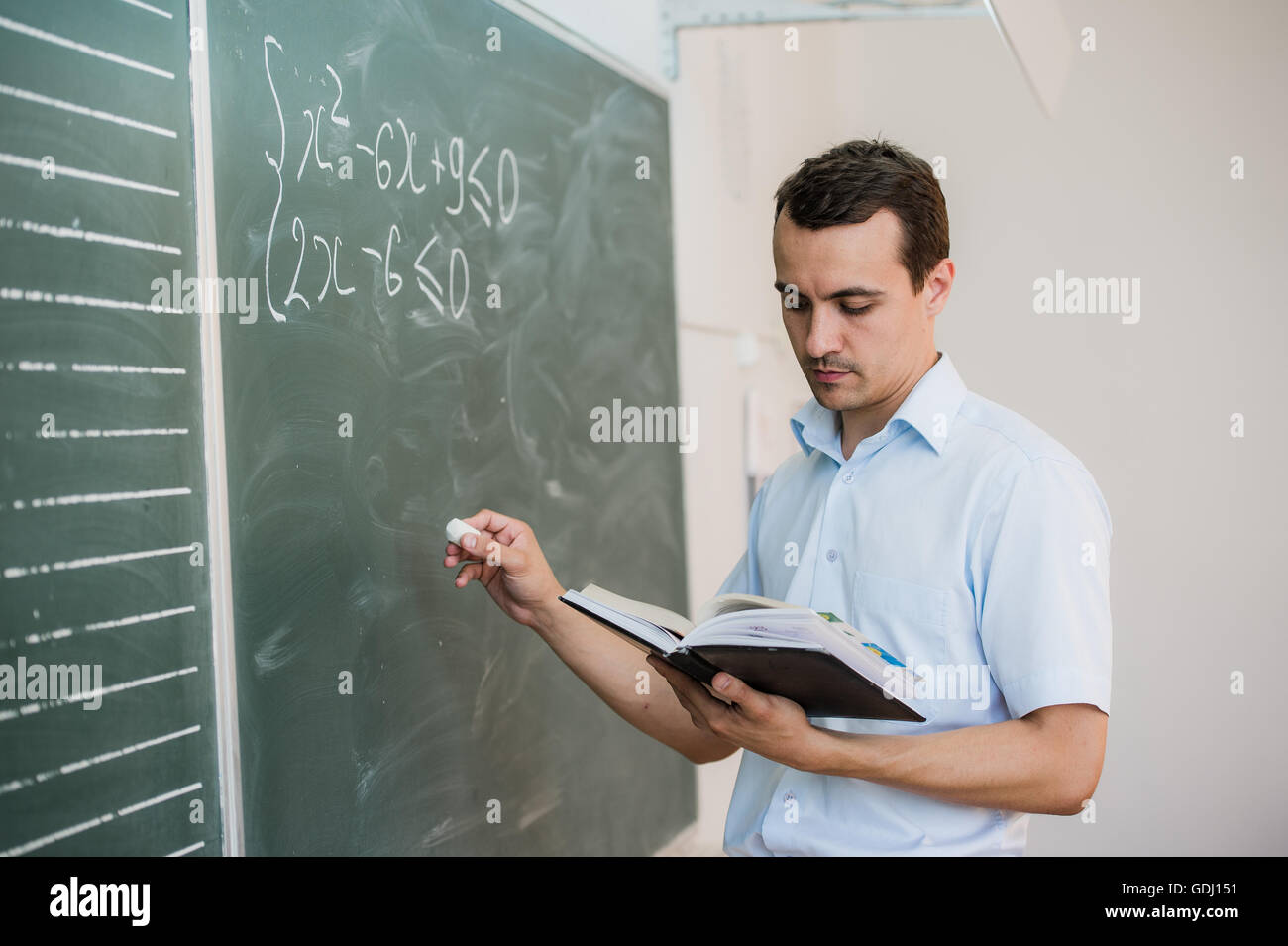 Junge männliche Lehrer oder Schüler mit Kreide schreiben an der Tafel im Klassenzimmer Stockfoto