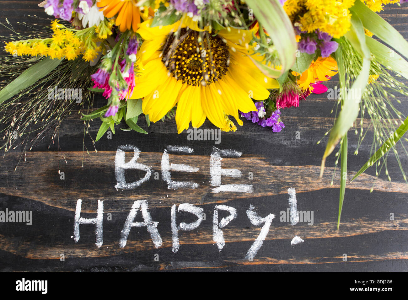Wörter-Biene glücklich mit Sommerblumen auf einem rustikalen hölzernen Hintergrund. Stockfoto