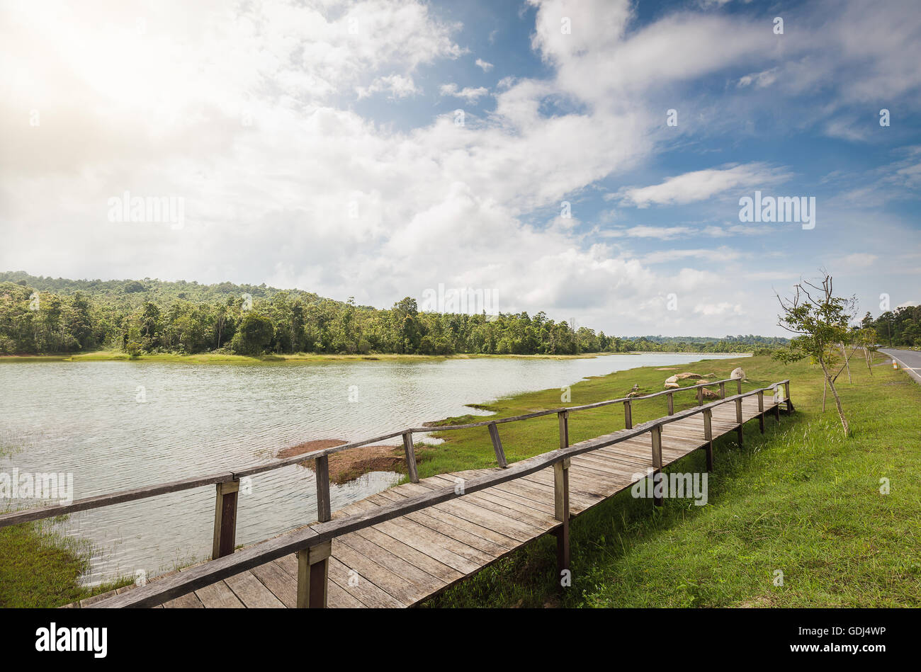 Holzbrücke über Überschwemmungsgebiet des großen Sees die grünen Rasen Land verbinden, daß Wald mit sonnigen blauen Himmel als Hinterg Stockfoto