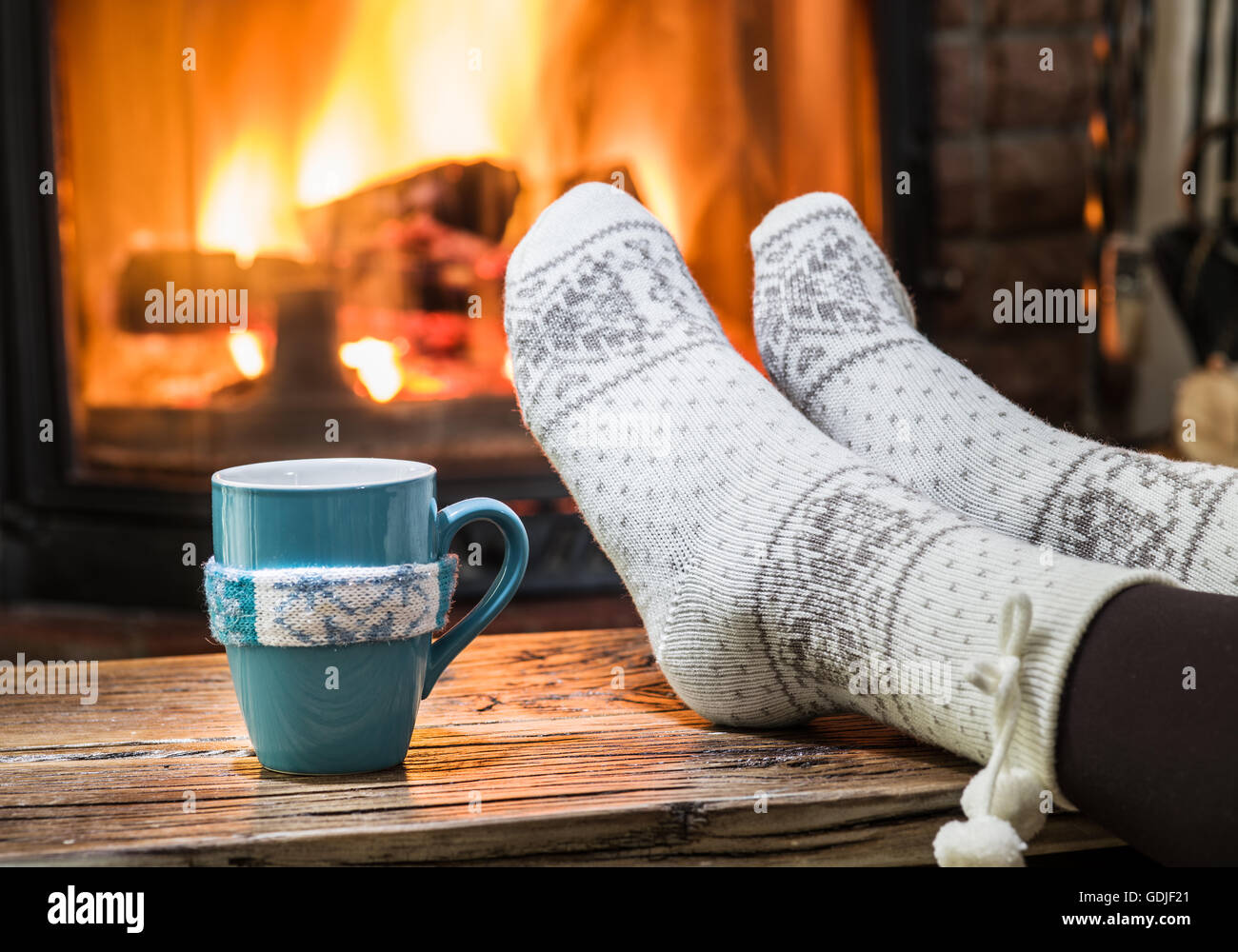 Wärmend und entspannend in der Nähe von Kamin. Frau Füße in der Nähe von der Tasse heißes Getränk am Kamin. Stockfoto