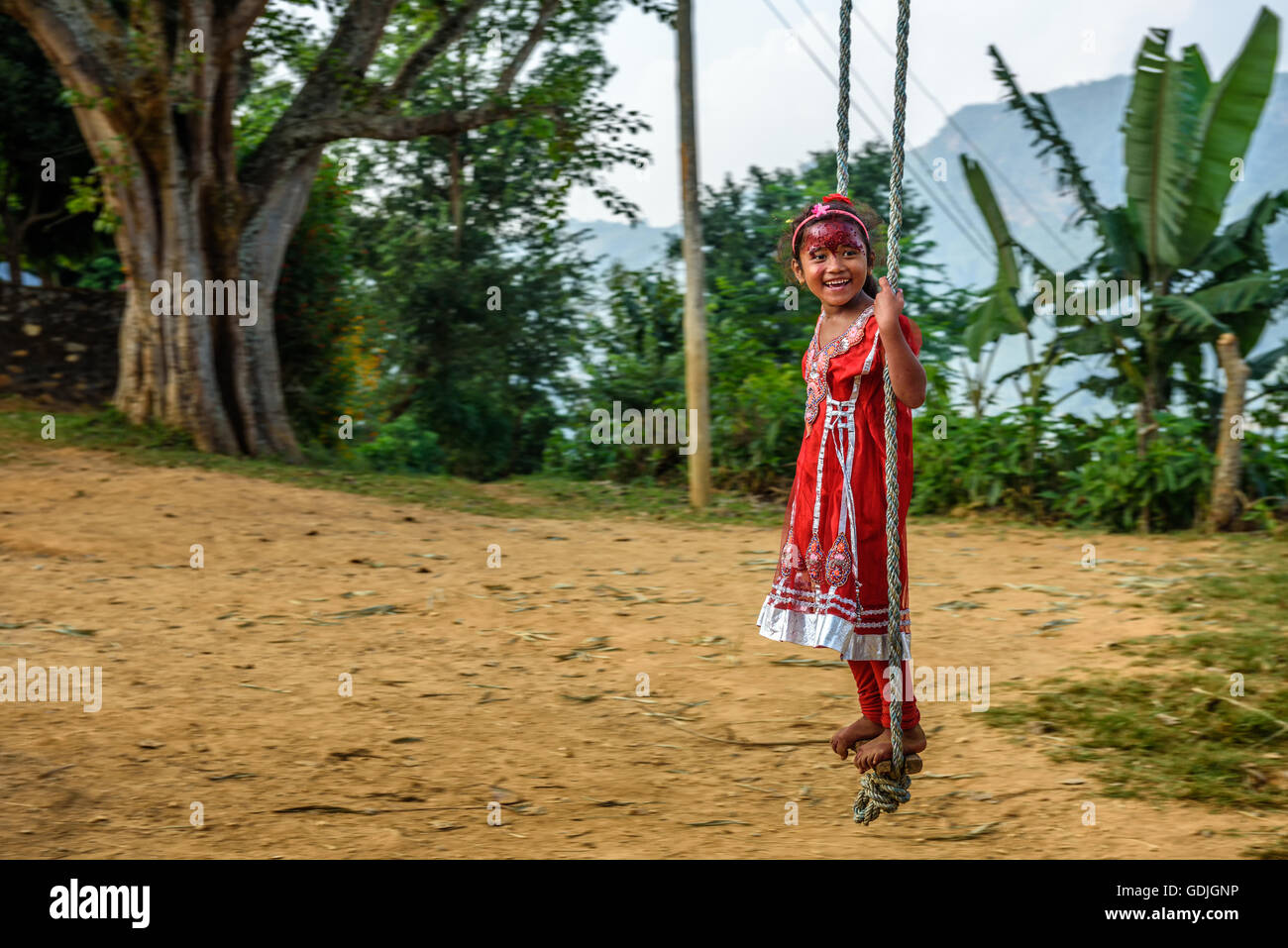 Nepalesische Mädchen im roten Kleid spielt auf einem traditionellen Bambus Schaukel genannt Linge Ping. Stockfoto
