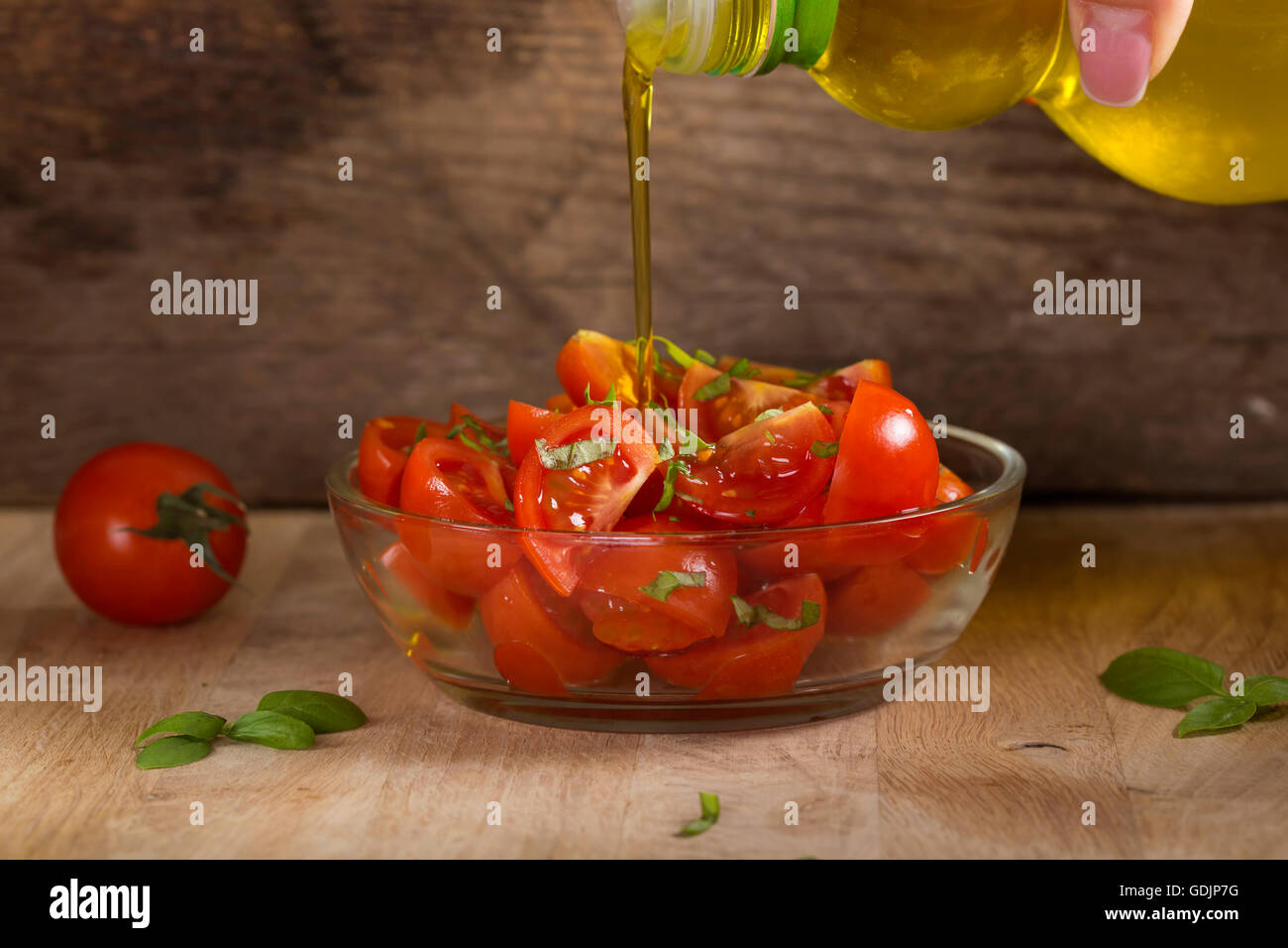 Gießen Olivenöl über Tomatenscheiben in Schüssel auf alten rustikalen hölzernen Hintergrund Stockfoto