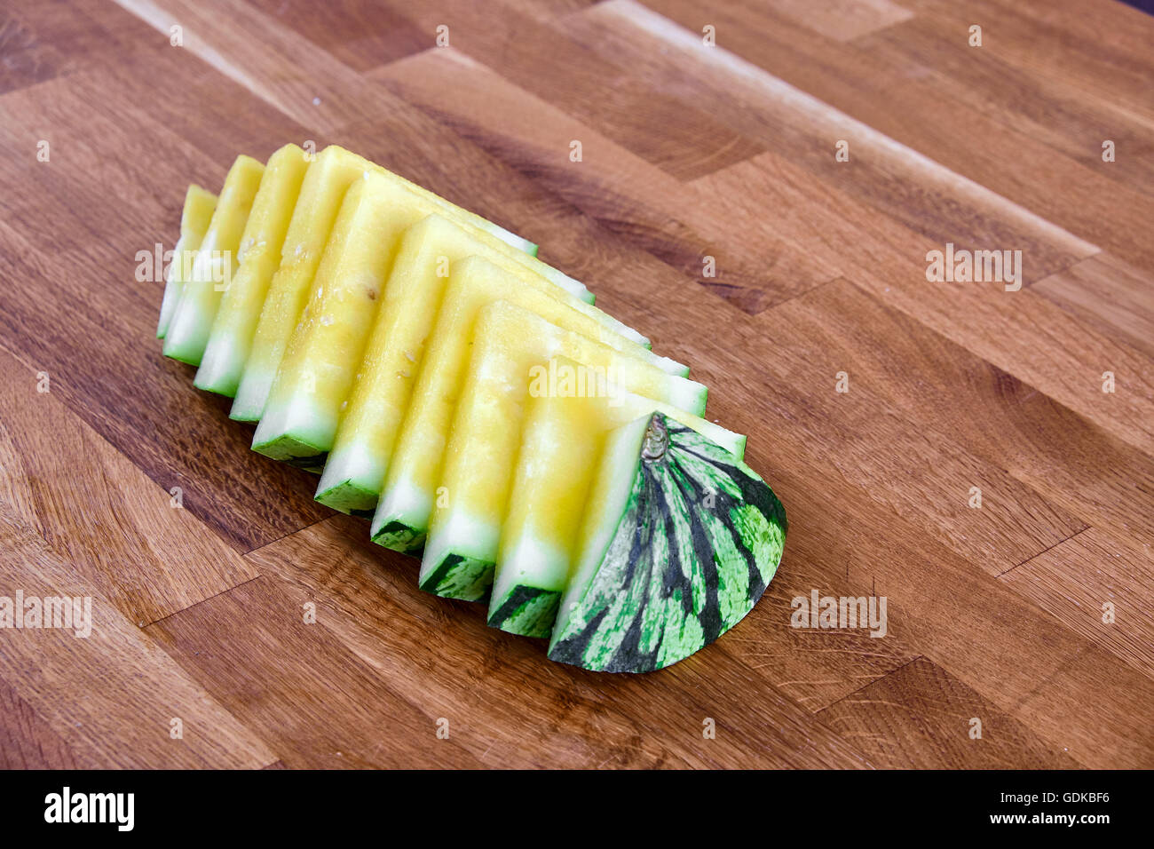 Gelbe Wassermelone in Scheiben geschnitten in Stücke, liegen auf einem Tisch von dunklen braunen laminiertem Hartholz Stockfoto