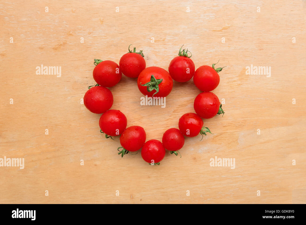 Cherry-Tomate frisch in Herzform auf Schneidbrett aus Holz, lag flach Stockfoto