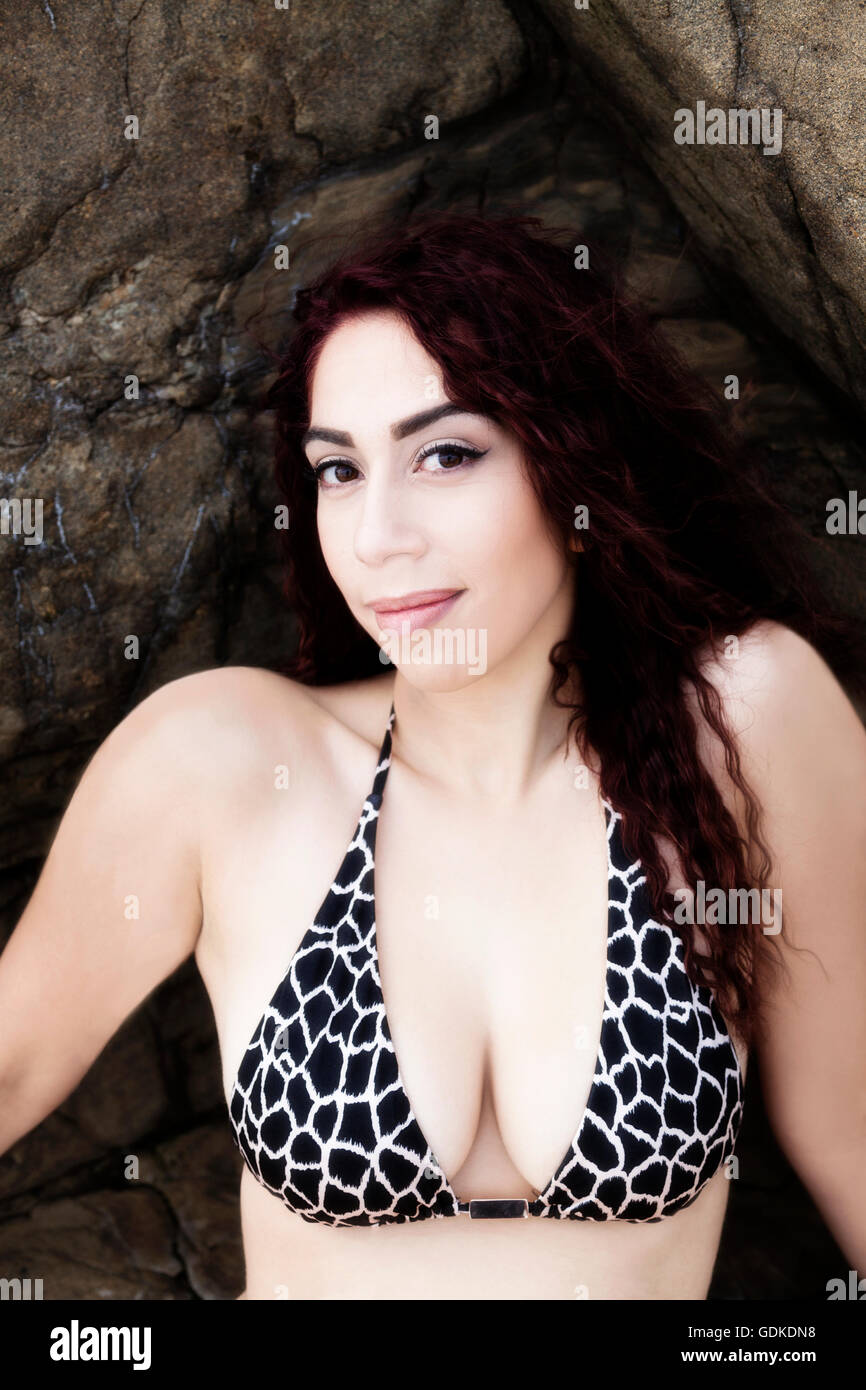 Hispanic Frau im Bikini Top sitzen auf den Felsen im Freien zeigt Dekolleté Stockfoto