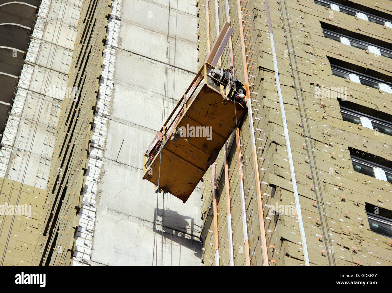 Bau unterbrochen gelbe Wiege mit Arbeitern auf einem neu gebauten Hochhaus Stockfoto