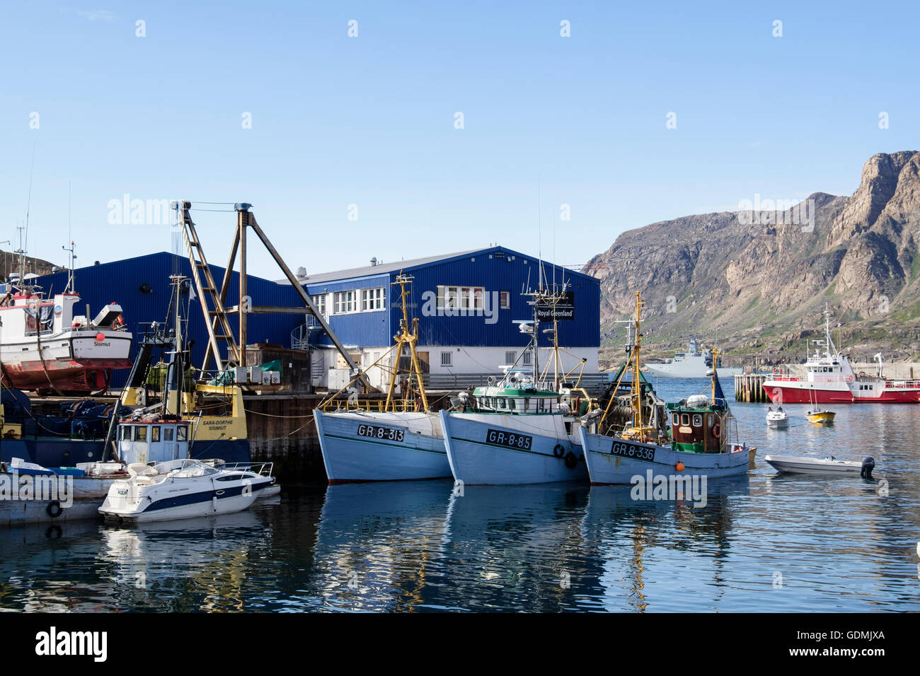 Grönländische Angelboote/Fischerboote vertäut im Hafen mit blauen Royal Greenland Fisch Fabrikgebäude hinter. Sisimiut Westgrönland Stockfoto