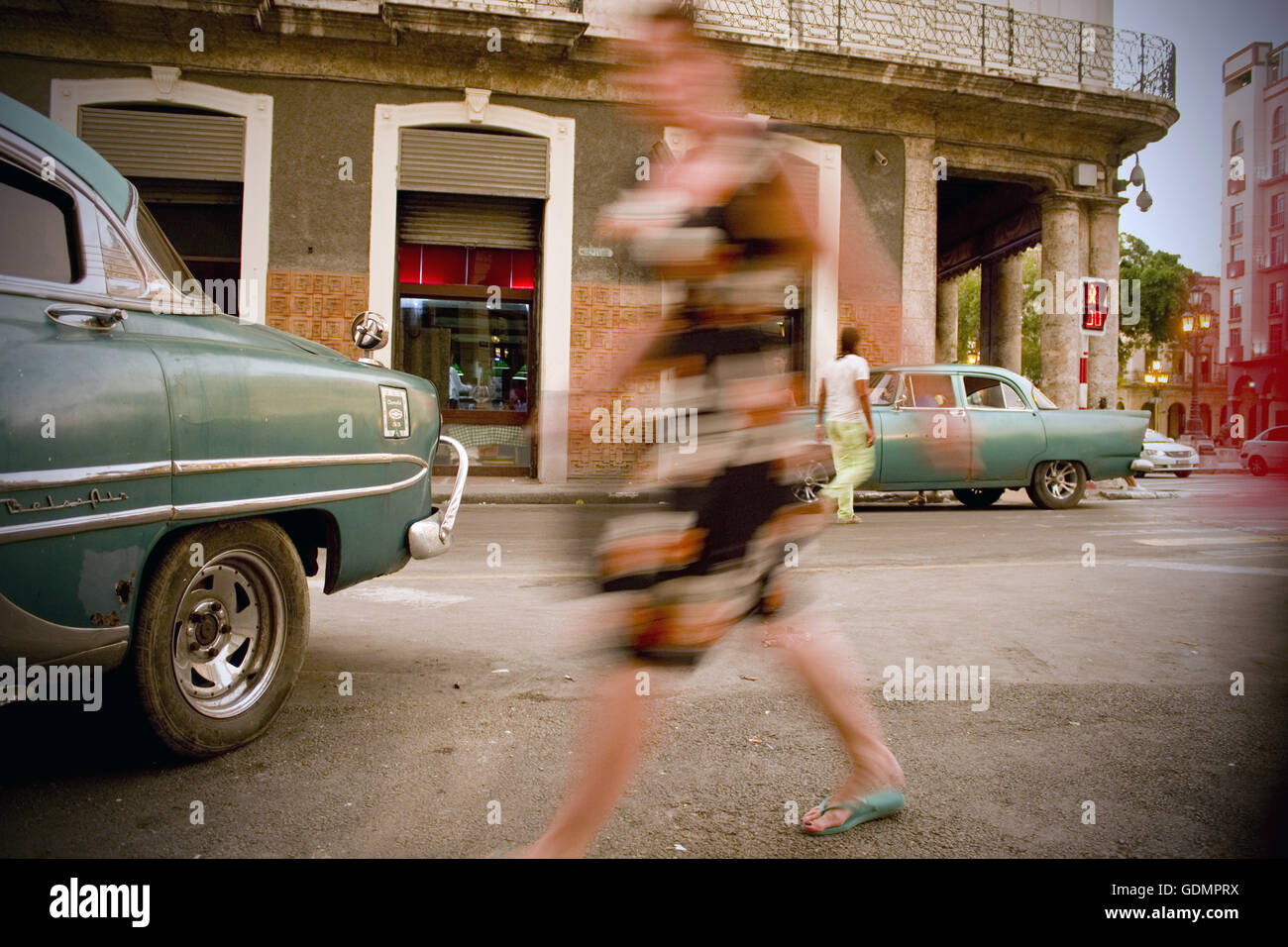 Slow-Motion Blur der Frau zu Fuß unter den klassischen alten Autos in der Innenstadt von Havanna, Kuba Stockfoto