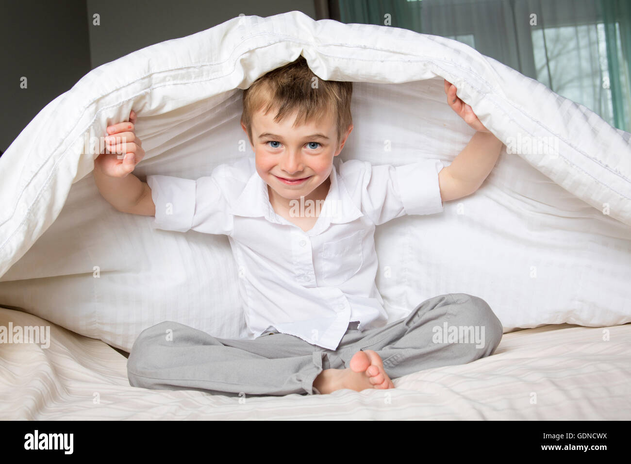 Lächelnde junge im Bett unter einer weißen Decke Tagesdecke versteckt. Stockfoto