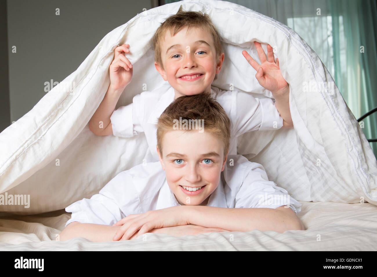 Junge im Bett unter einer weißen Decke Tagesdecke versteckt. Stockfoto
