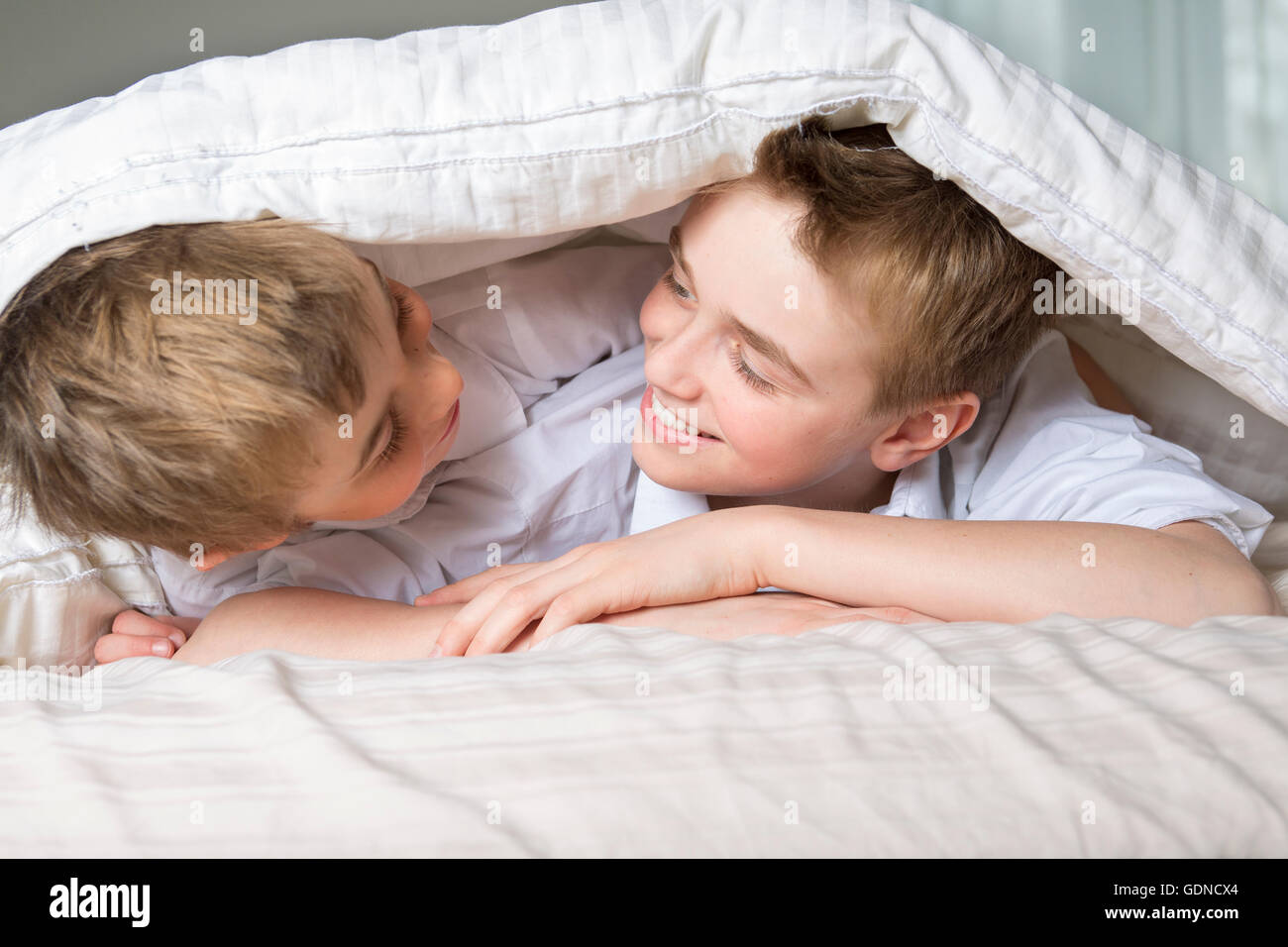 Junge im Bett unter einer weißen Decke Tagesdecke versteckt. Stockfoto