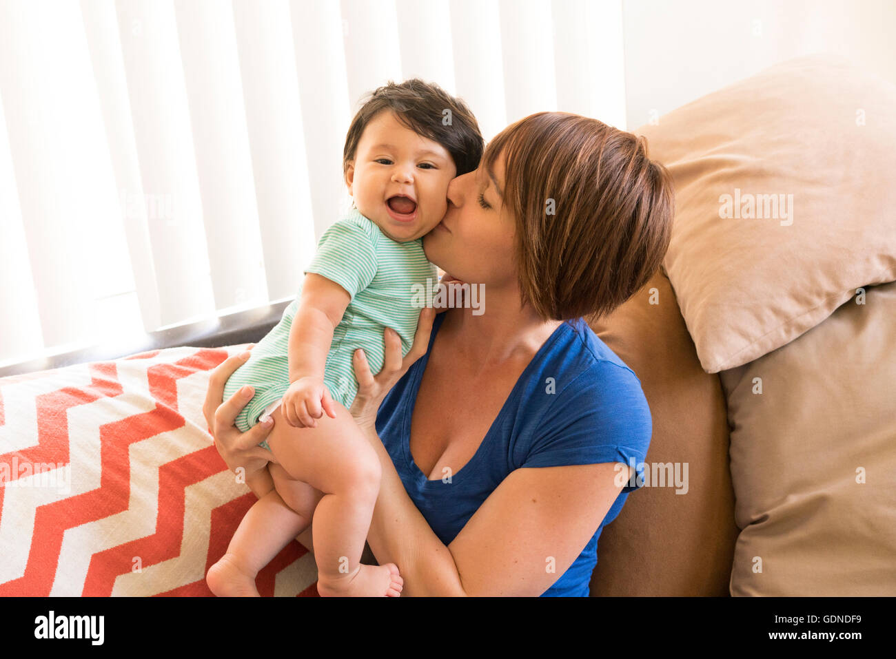 Mutter auf Sofa Babys Wange küssen Stockfoto