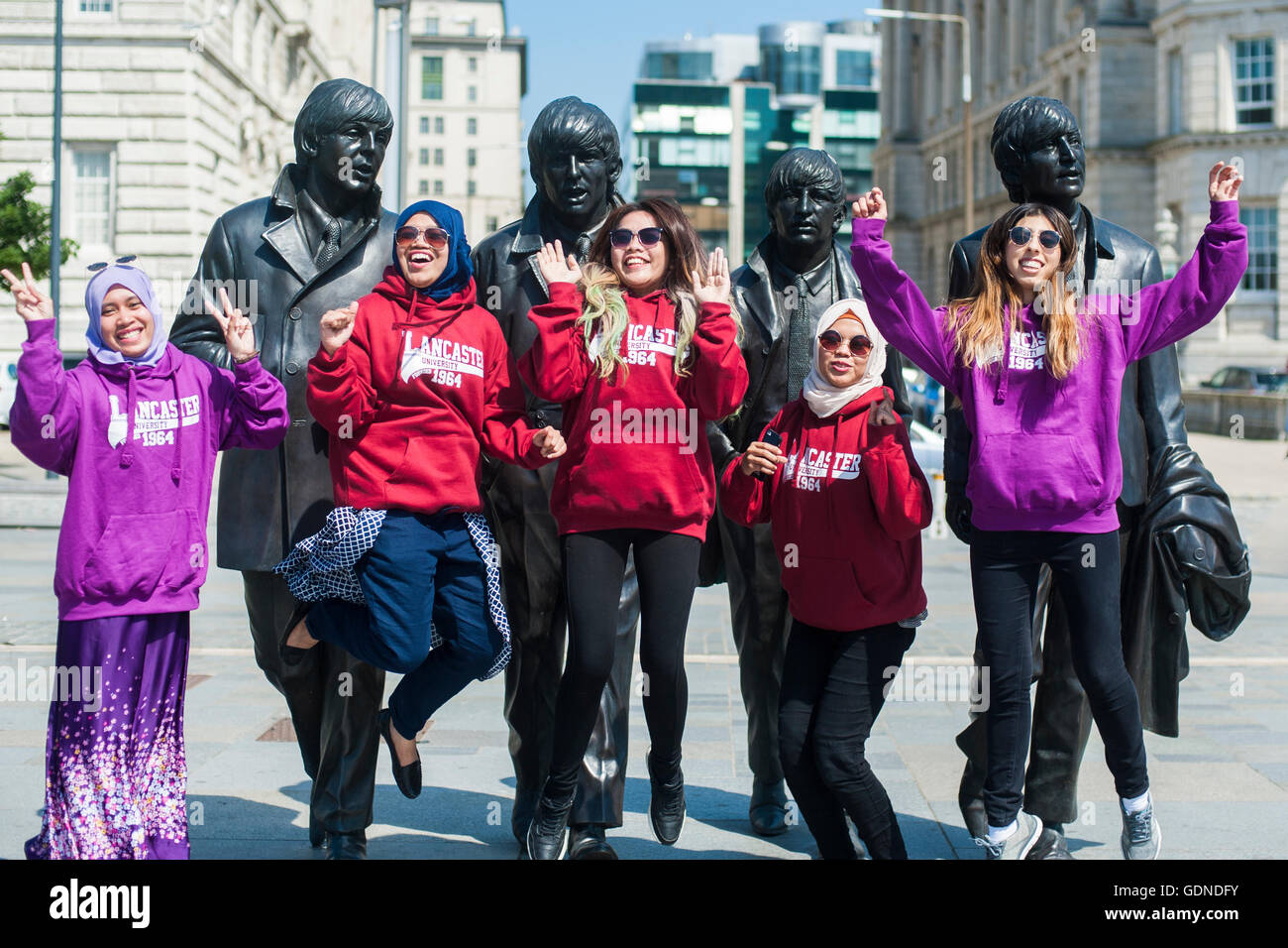 Eine Gruppe von glücklichen jungen Studenten der verschiedenen ethnischen Minderheiten Aufspringen vor den Beatles Statuen in Liverpool UK Stockfoto