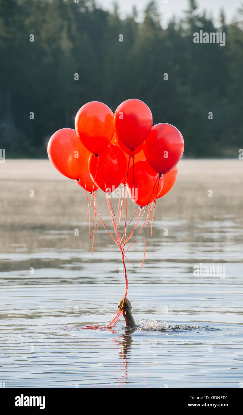 Hand im Wasser halten Haufen rote Luftballons Stockfoto