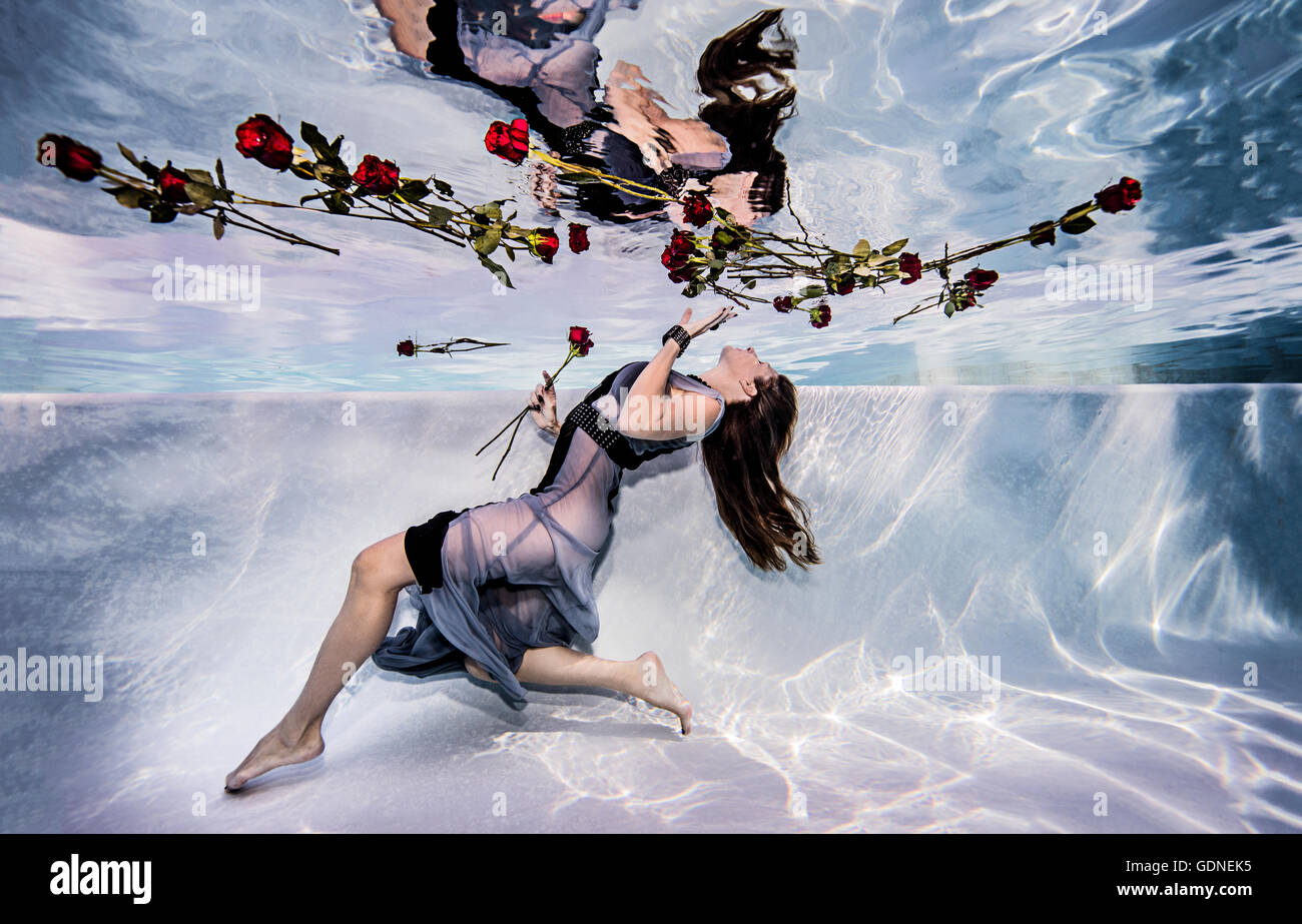 Frau trägt Kleid unter Wasser im Schwimmbad mit Rosen Stockfoto