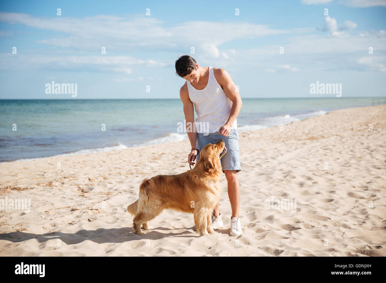 Hübscher junger Mann stehen und spielen mit seinem Hund am Strand Stockfoto