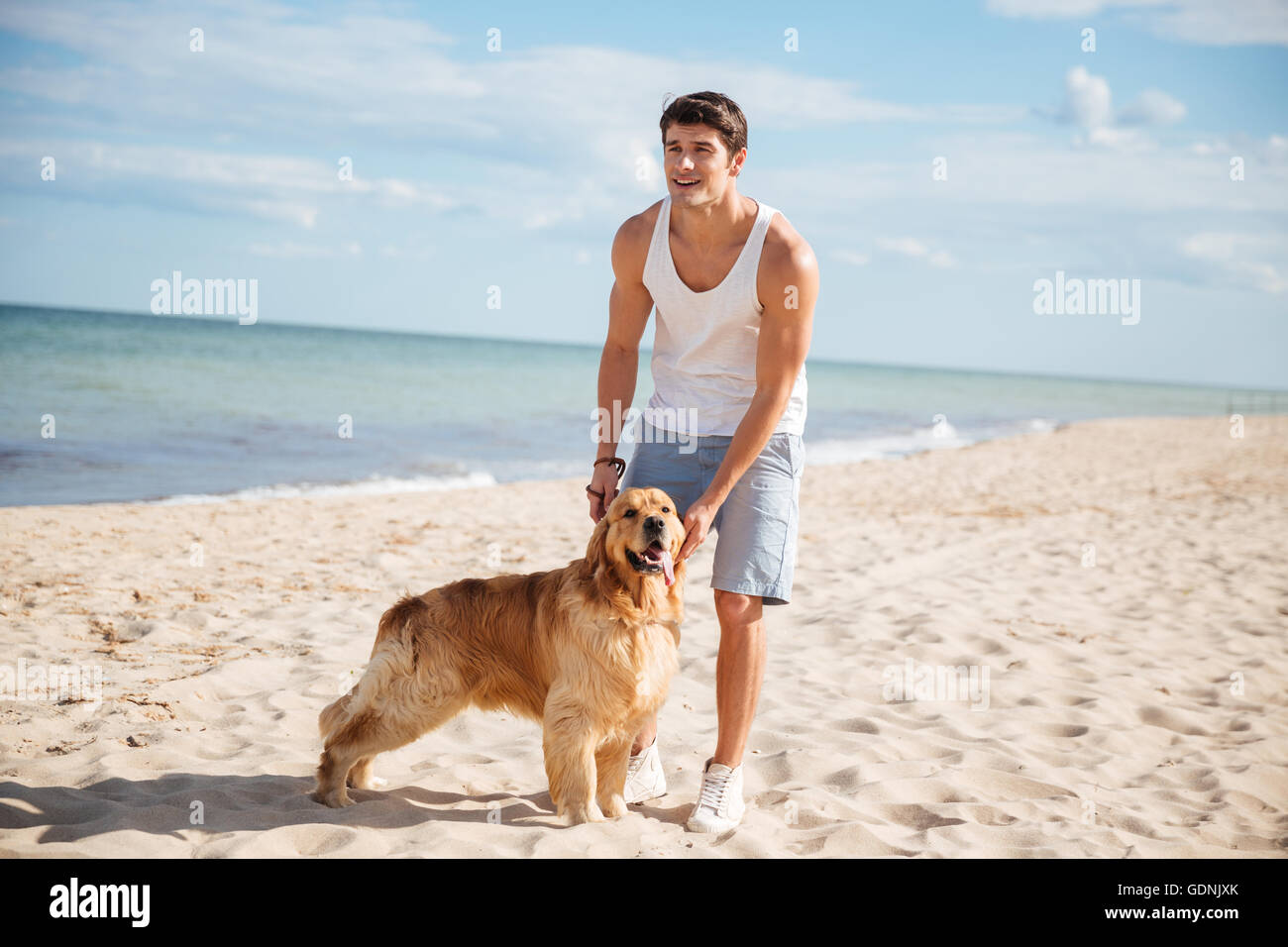 Glücklich attraktive junge Mann zu Fuß und spielen mit seinem Hund am Strand Stockfoto