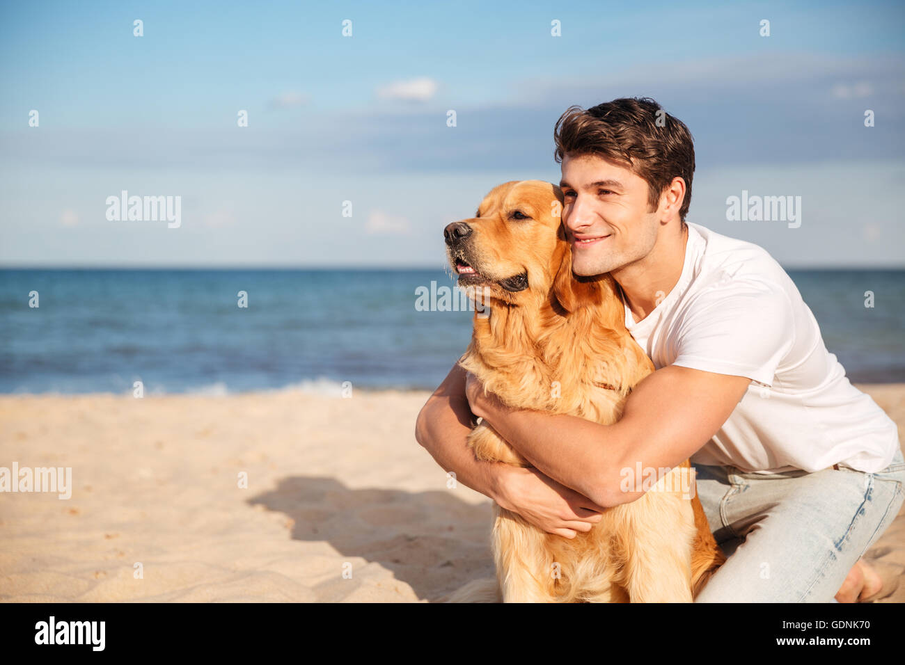 Lächelnd attraktive jungen Mann umarmt seinen Hund am Strand im Sommer Stockfoto