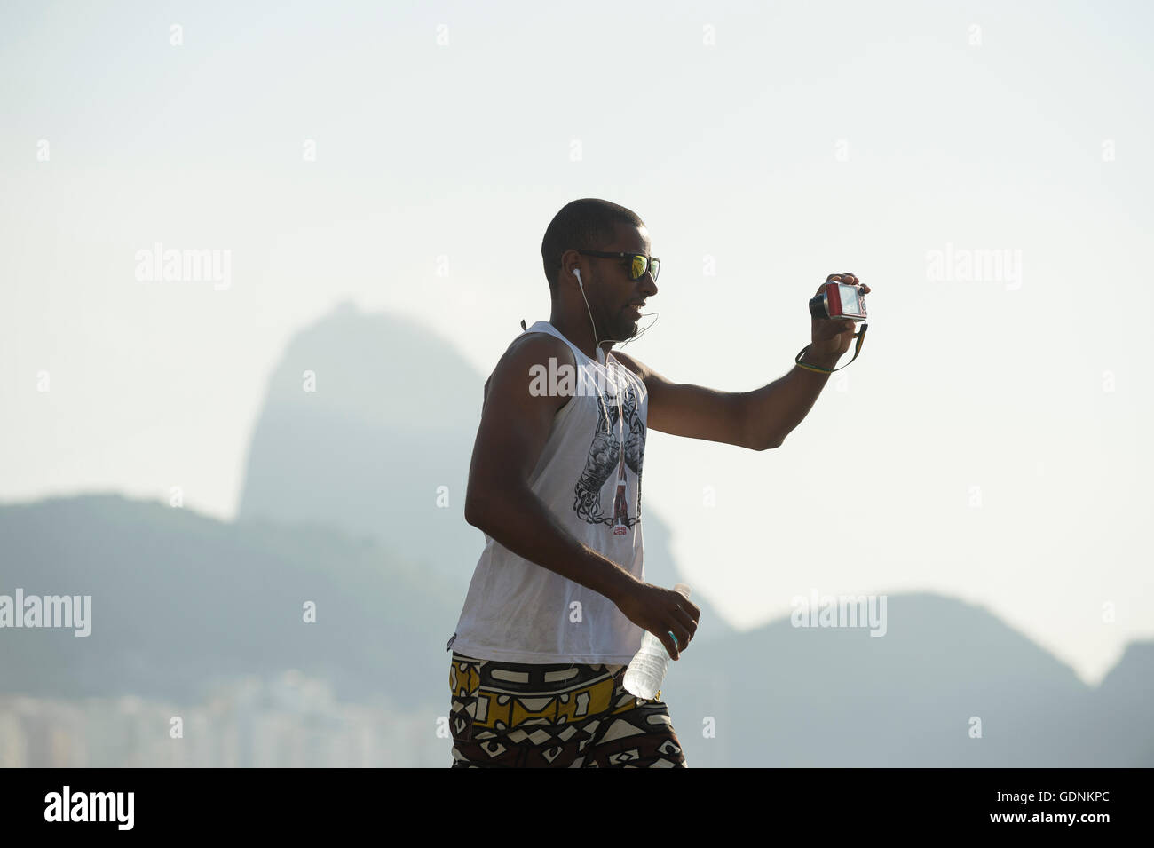 RIO DE JANEIRO - 3. April 2016: Eine junge Carioca brasilianischen Mann hält eine Kamera bis zu nehmen ein Selfie beim Joggen entlang der Copacabana. Stockfoto
