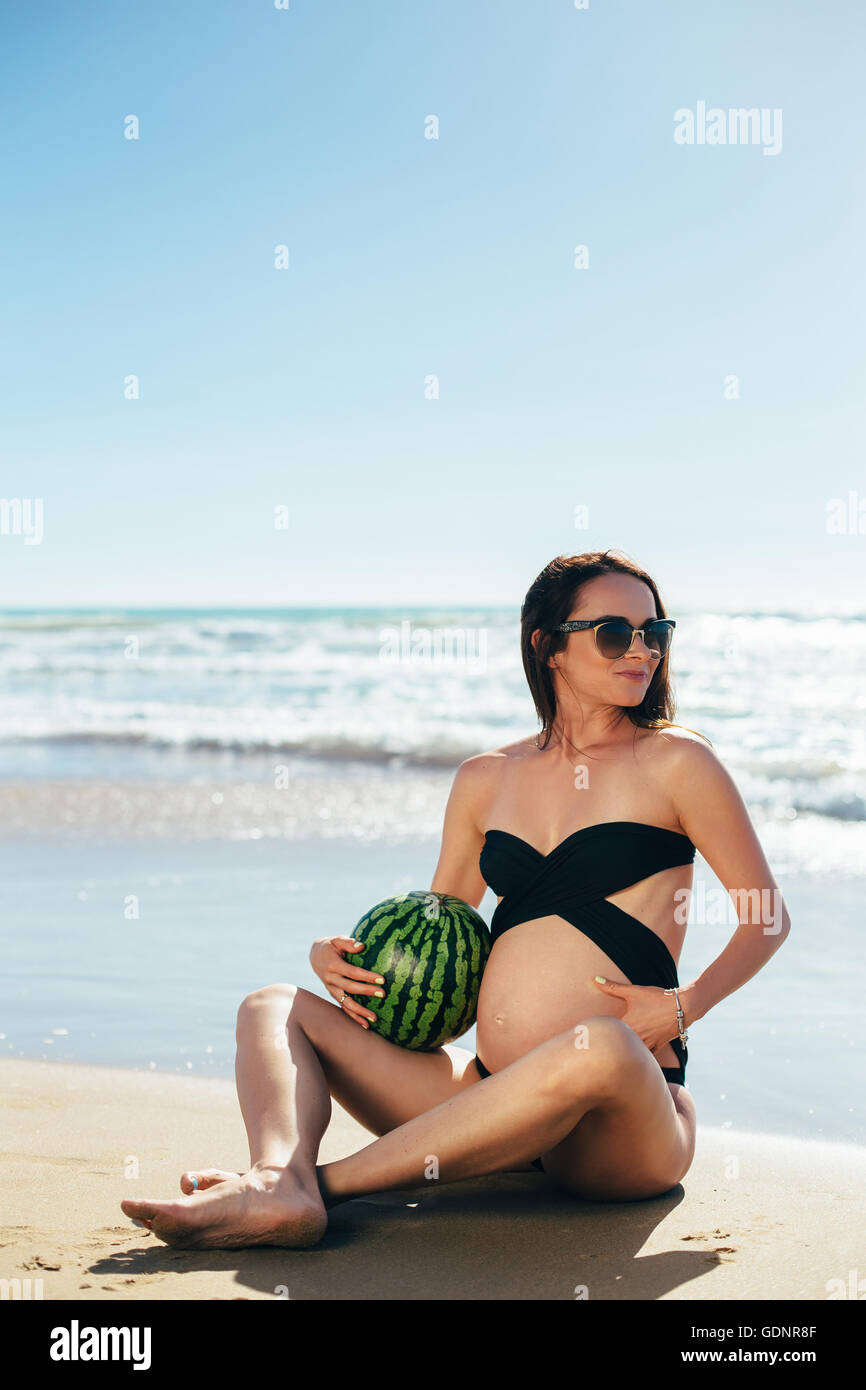 Werdende Mutter mit Wassermelone am Strand Stockfoto