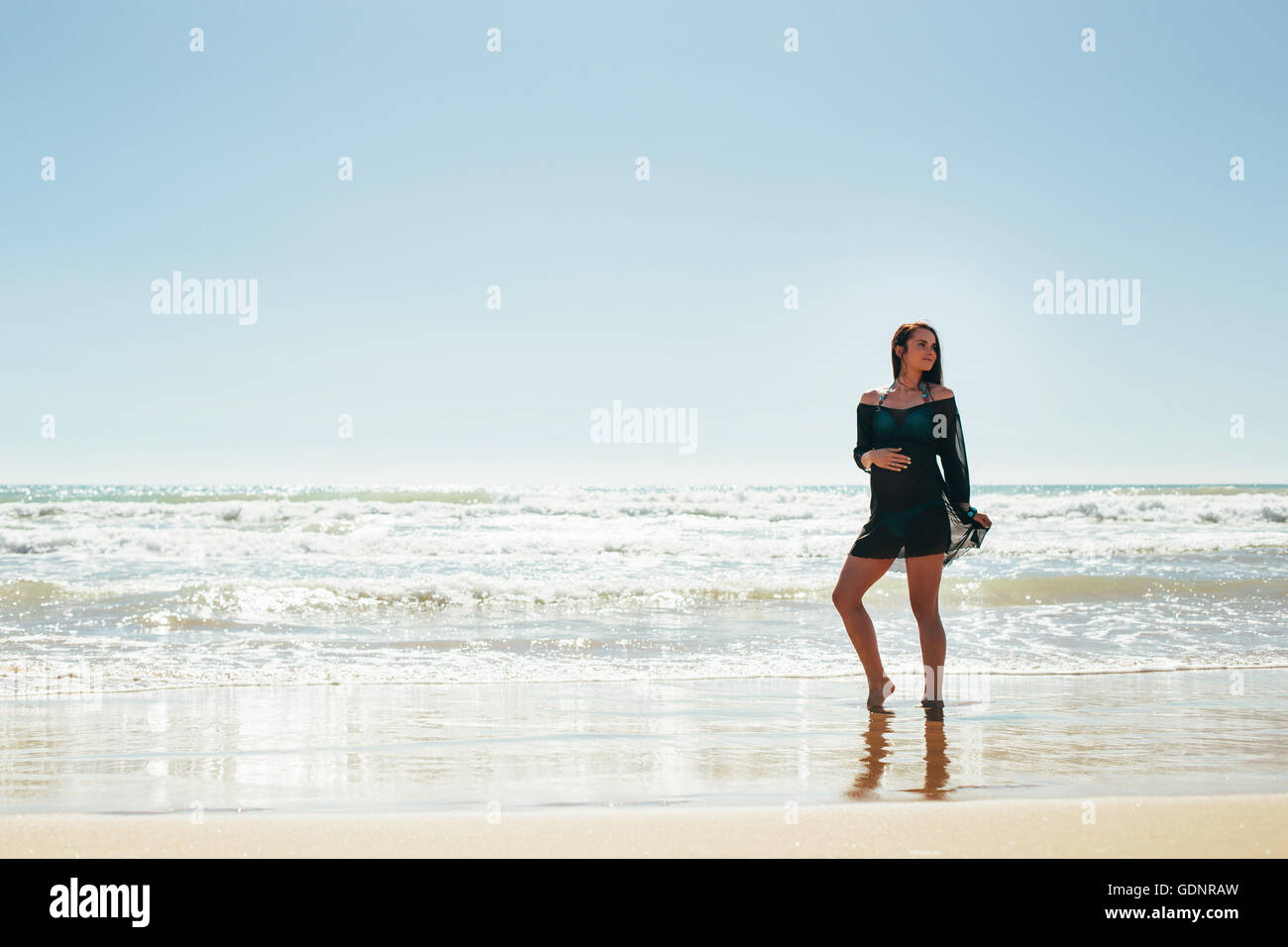 Schwangere Frau posiert am Strand Stockfoto