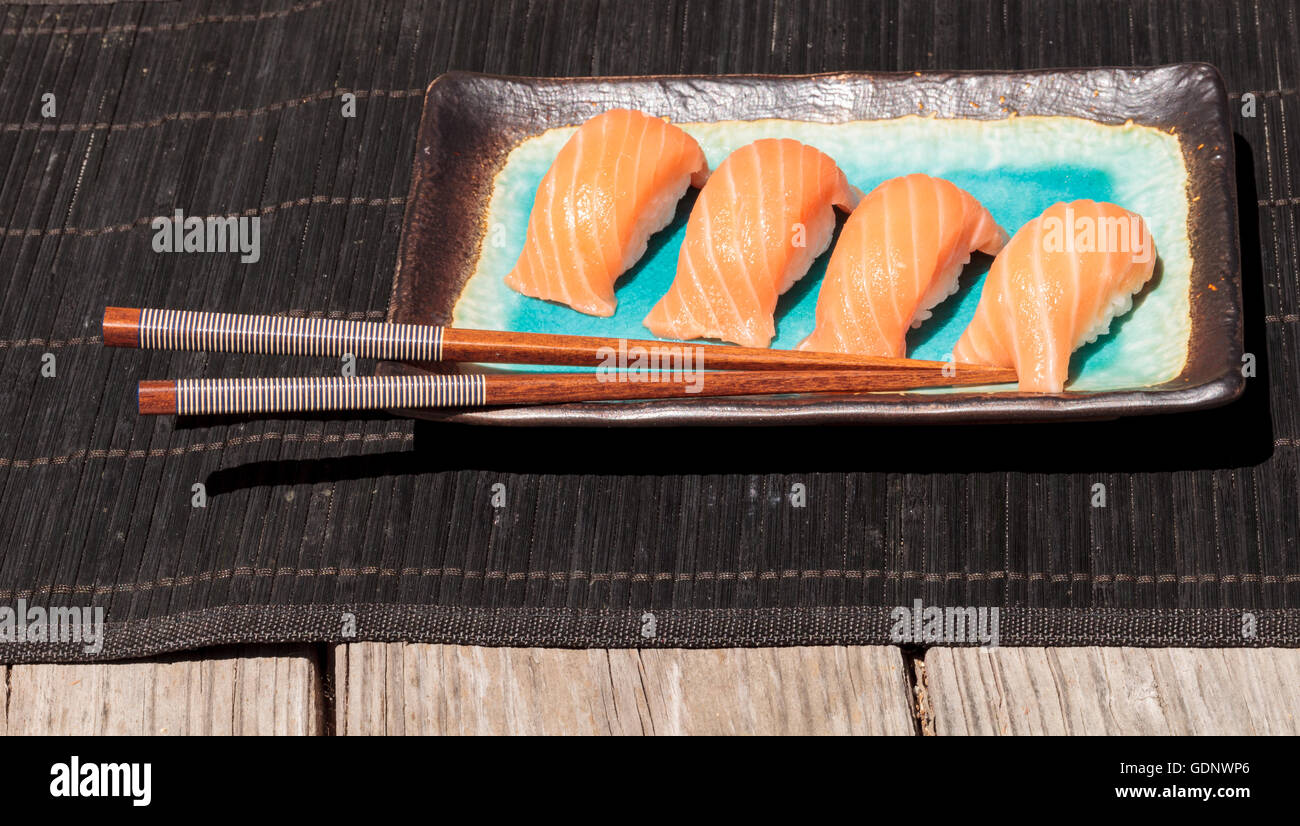 Eine Mahlzeit mit Lachs Sushi auf weißem Reis auf einem blauen Teller mit Stäbchen. Stockfoto