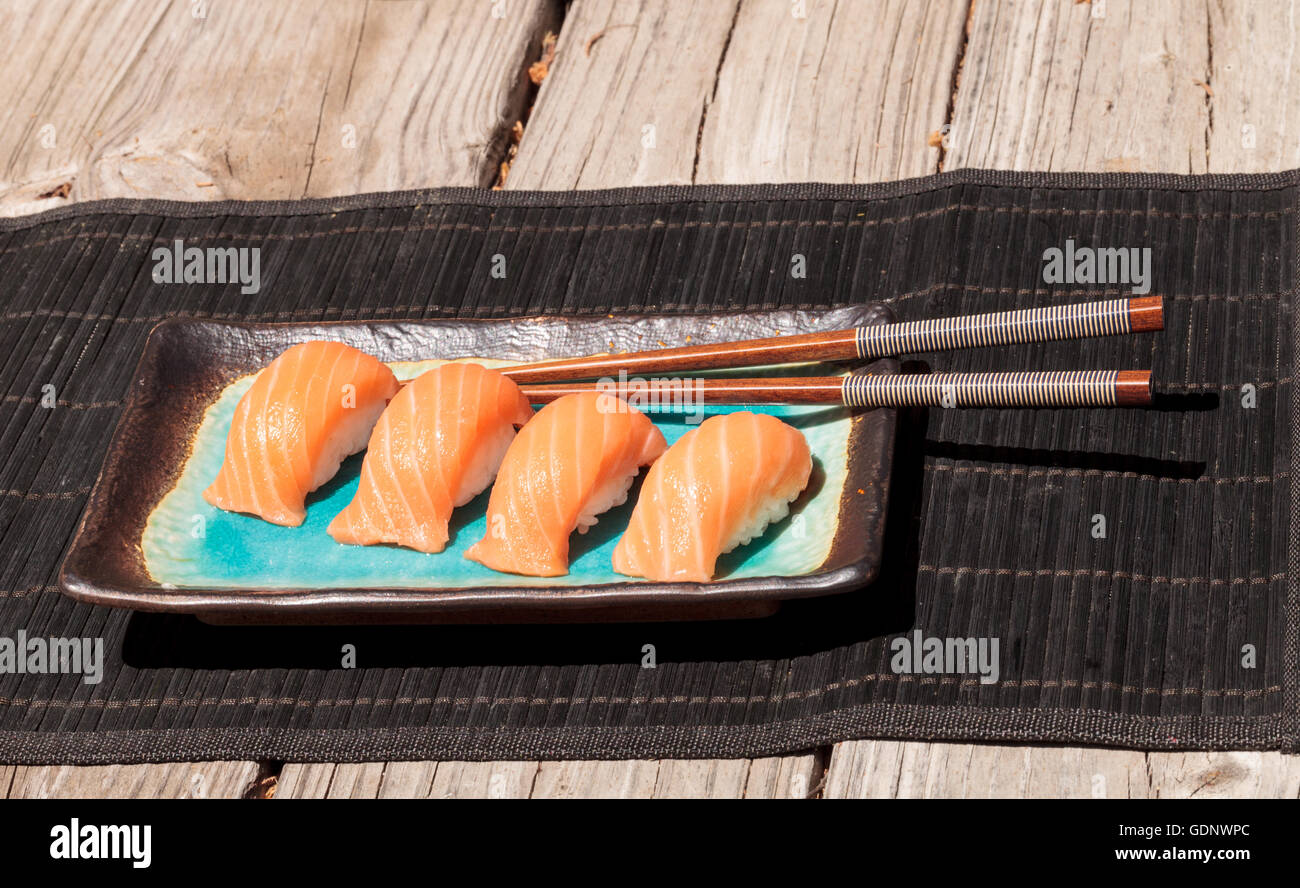 Eine Mahlzeit mit Lachs Sushi auf weißem Reis auf einem blauen Teller mit Stäbchen. Stockfoto