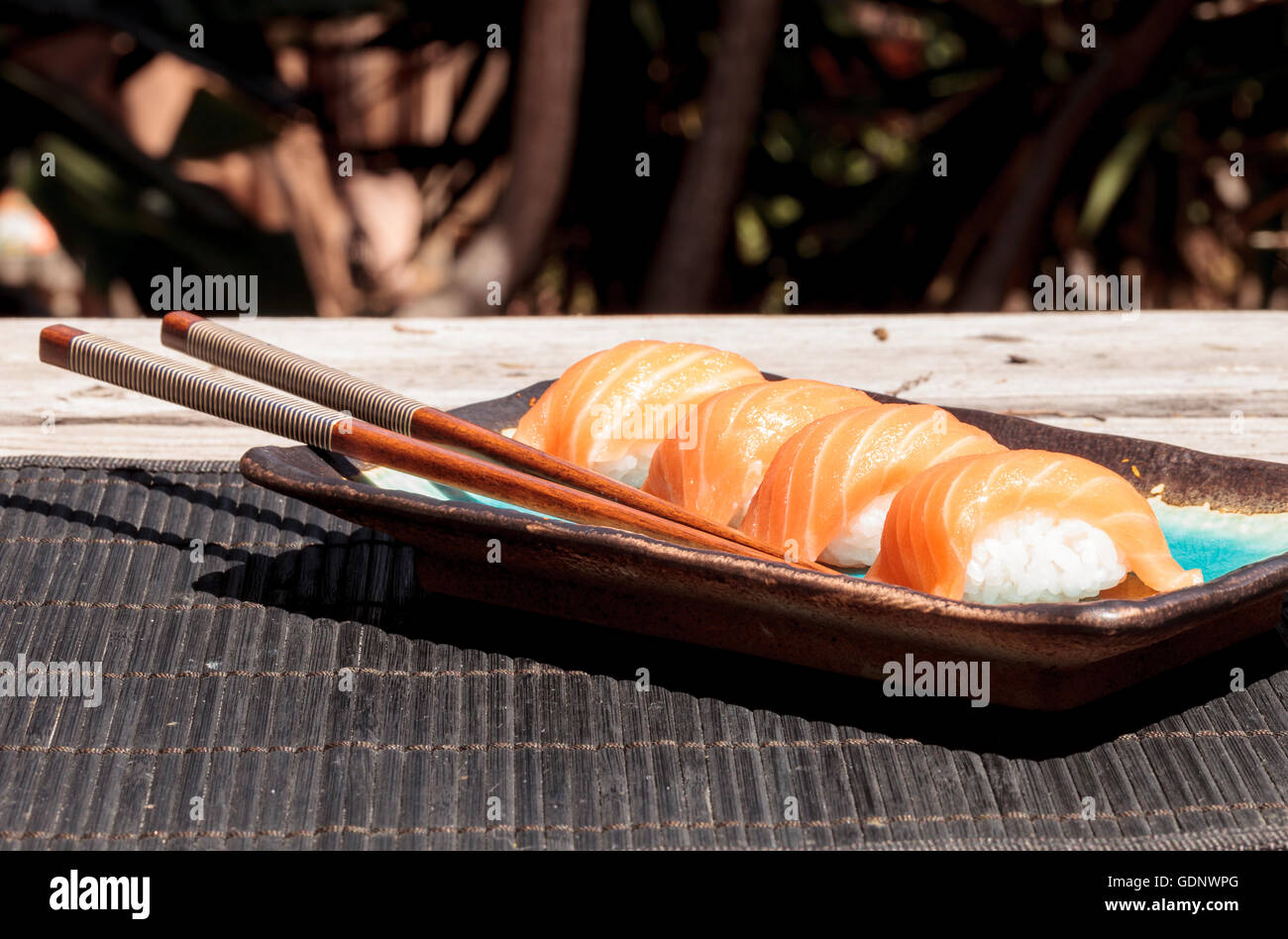Eine Mahlzeit mit Lachs Sushi auf weißem Reis auf einem blauen Teller mit Stäbchen. Stockfoto