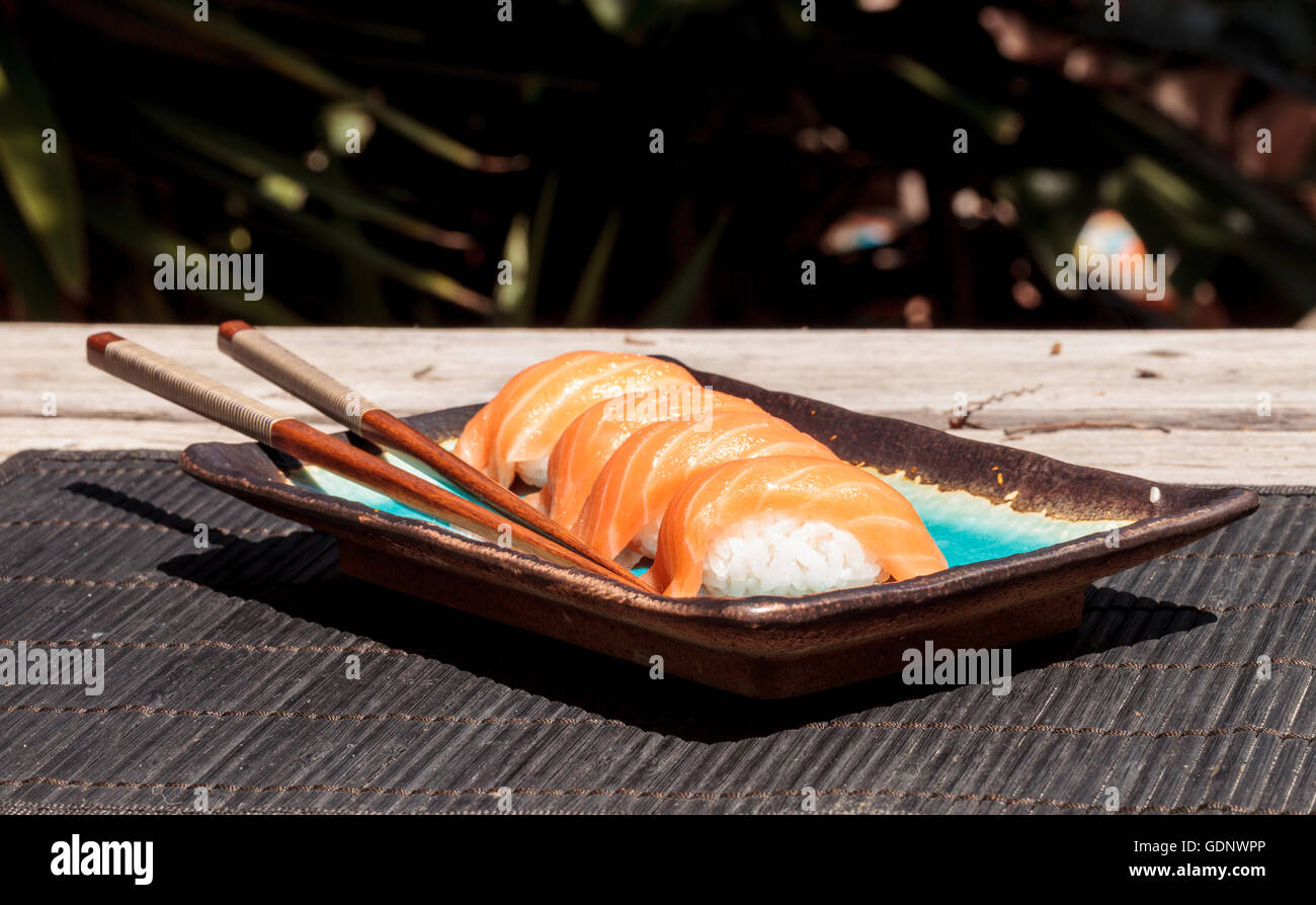 Eine Mahlzeit mit Lachs Sushi auf weißem Reis auf einem blauen Teller mit Stäbchen. Stockfoto