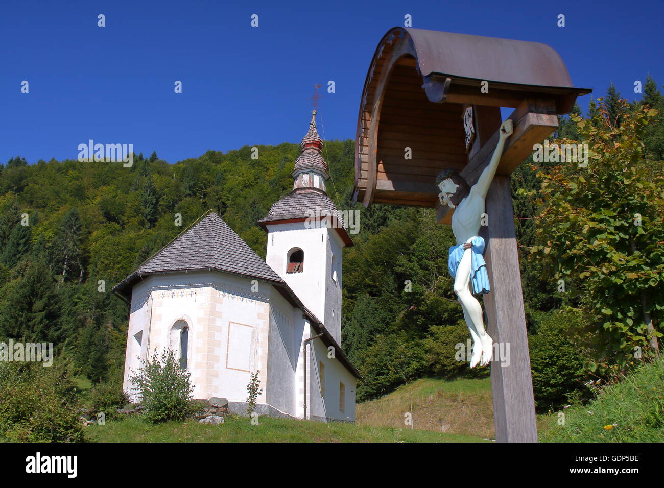 Einer traditionellen Kirche in Skofja Loka Hügeln mit Jesus Christus am Kreuz im Vordergrund, Slowenien Stockfoto