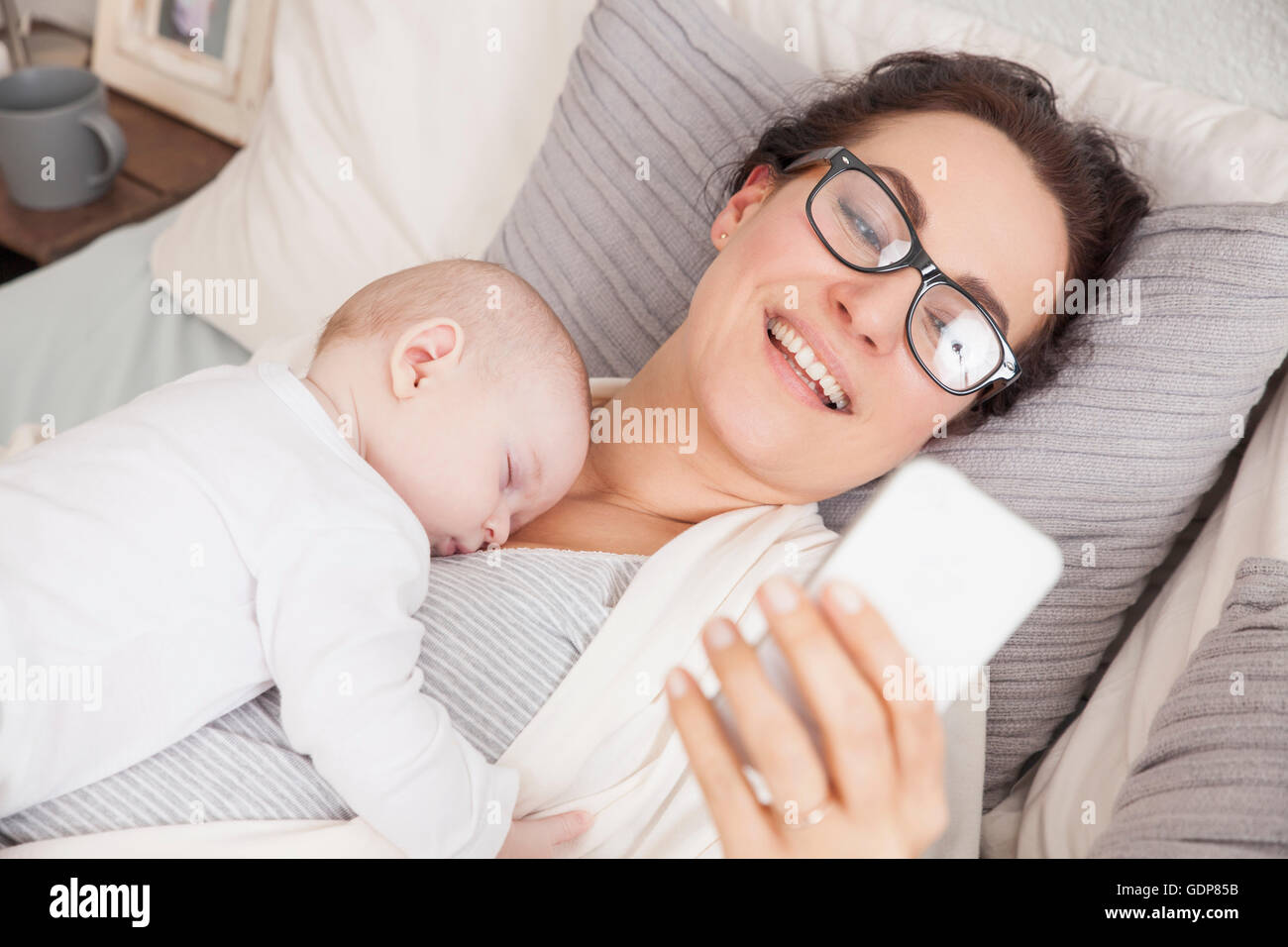 Babyjungen schlafen auf Mutter, Mutter mit smartphone Stockfoto