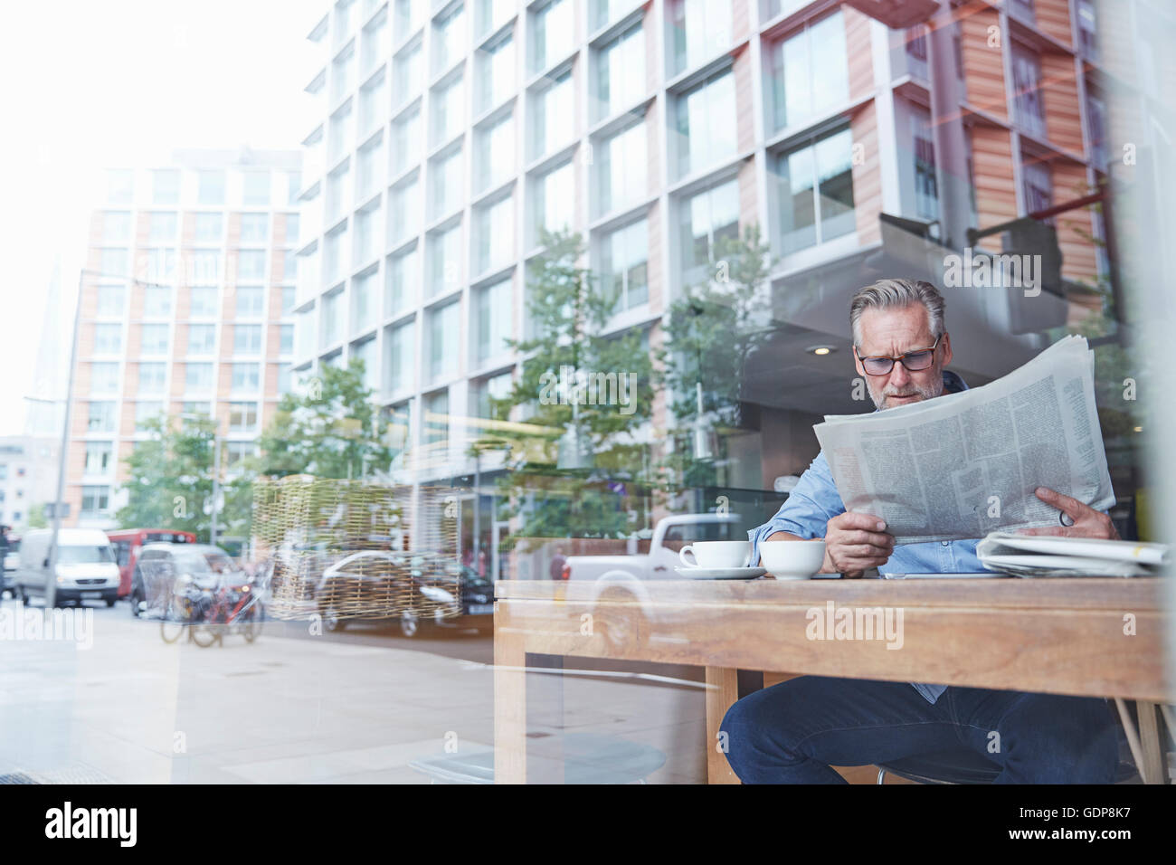 Reifer Mann sitzen im Café, lesen Zeitung, Straße spiegelt sich im Fenster Stockfoto