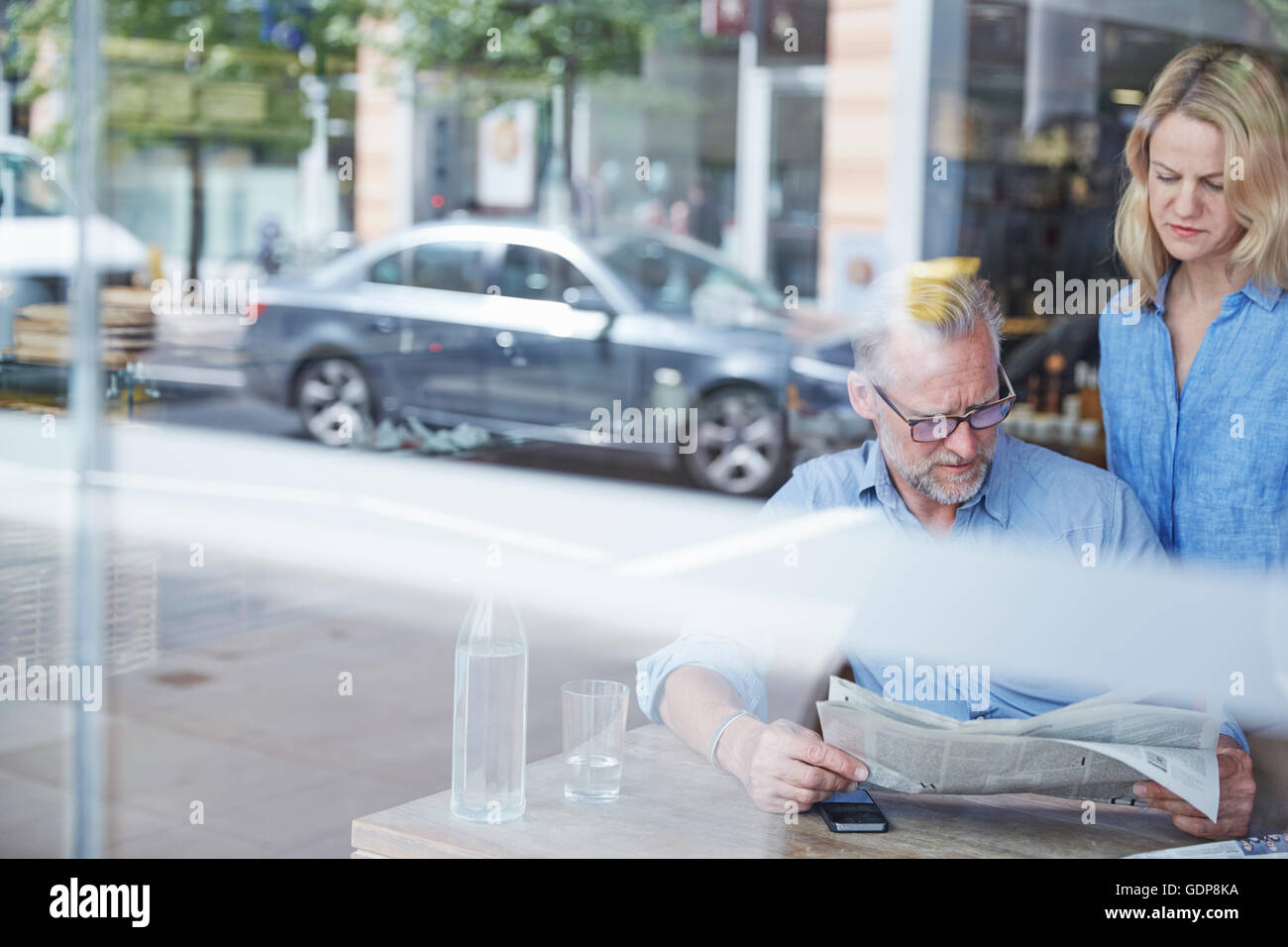 Reifer Mann und Frau in Café, liest Zeitung, Straße spiegelt sich im Fenster Stockfoto
