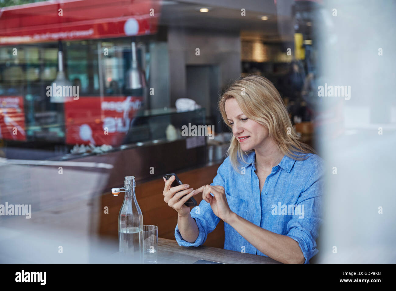 Reife Frau sitzen im Café, mit Smartphone, Bus spiegelt sich im Fenster Stockfoto