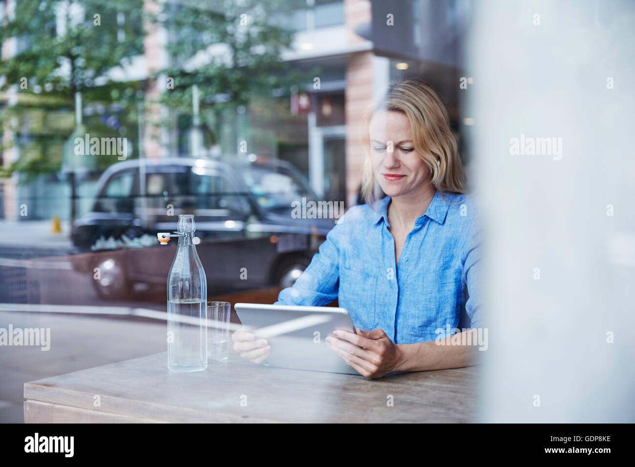 Reife Frau sitzen im Café, mit digital-Tablette, Taxi spiegelt sich im Fenster Stockfoto