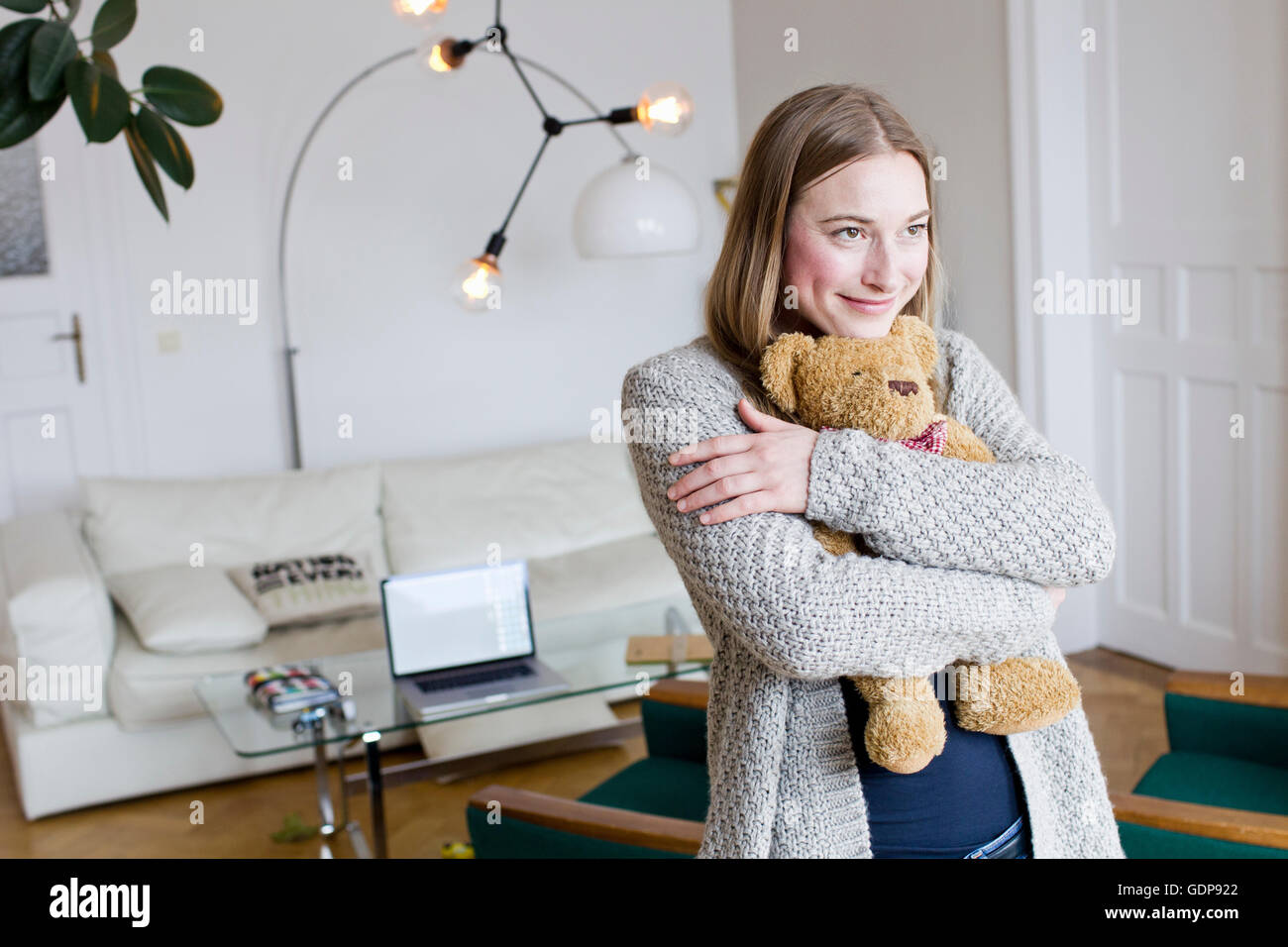 Mitte Erwachsene Frau umarmt Teddybär im Wohnzimmer Stockfoto