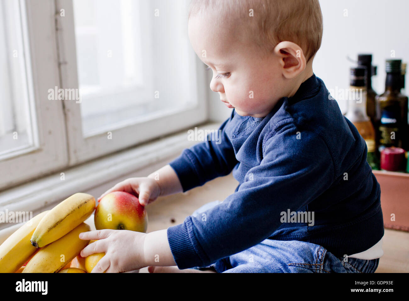 Baby Junge saß am Küchentisch spielen mit Obstschale Stockfoto